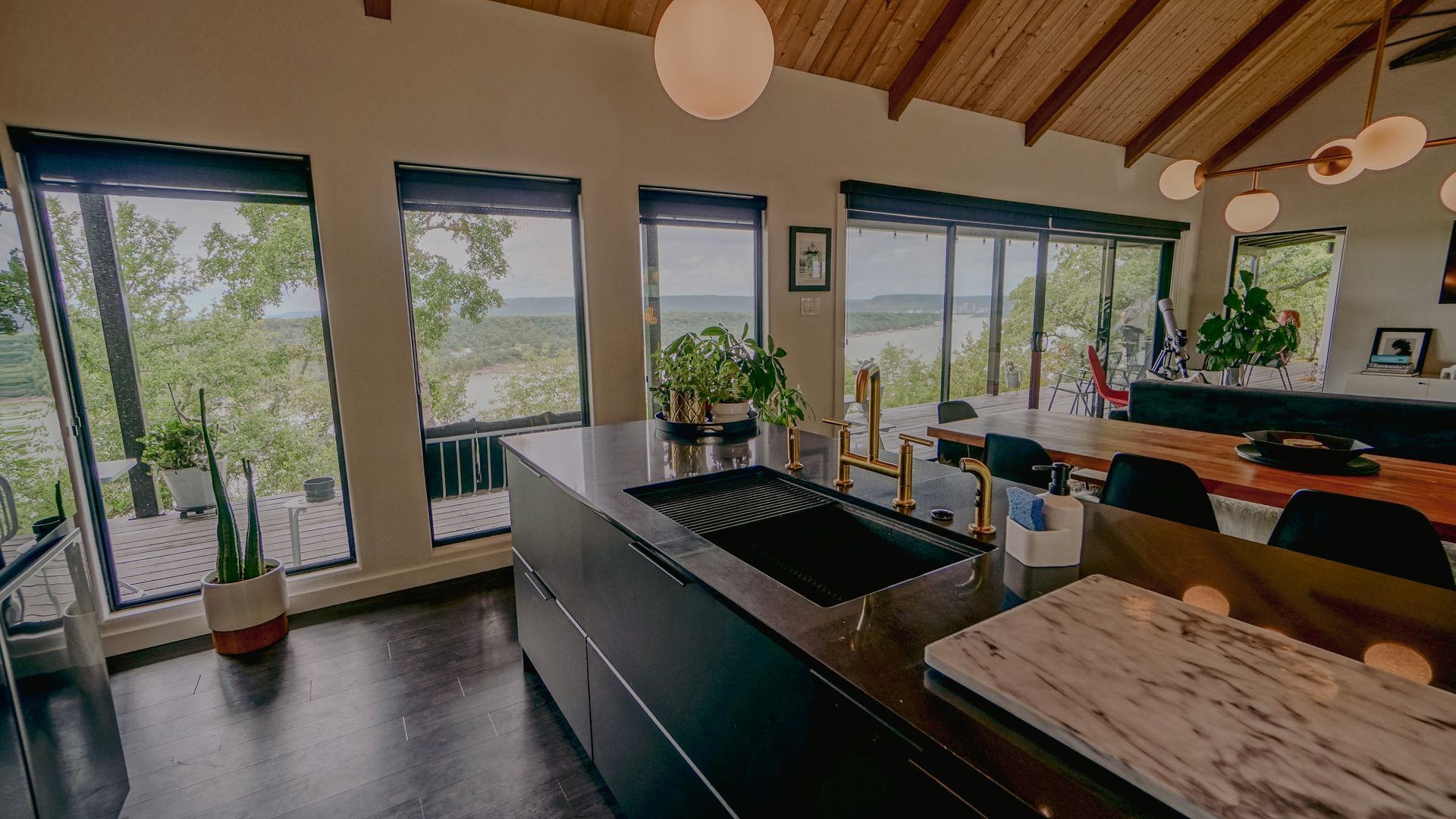 Modern kitchen with black island, large windows, and outdoor view.