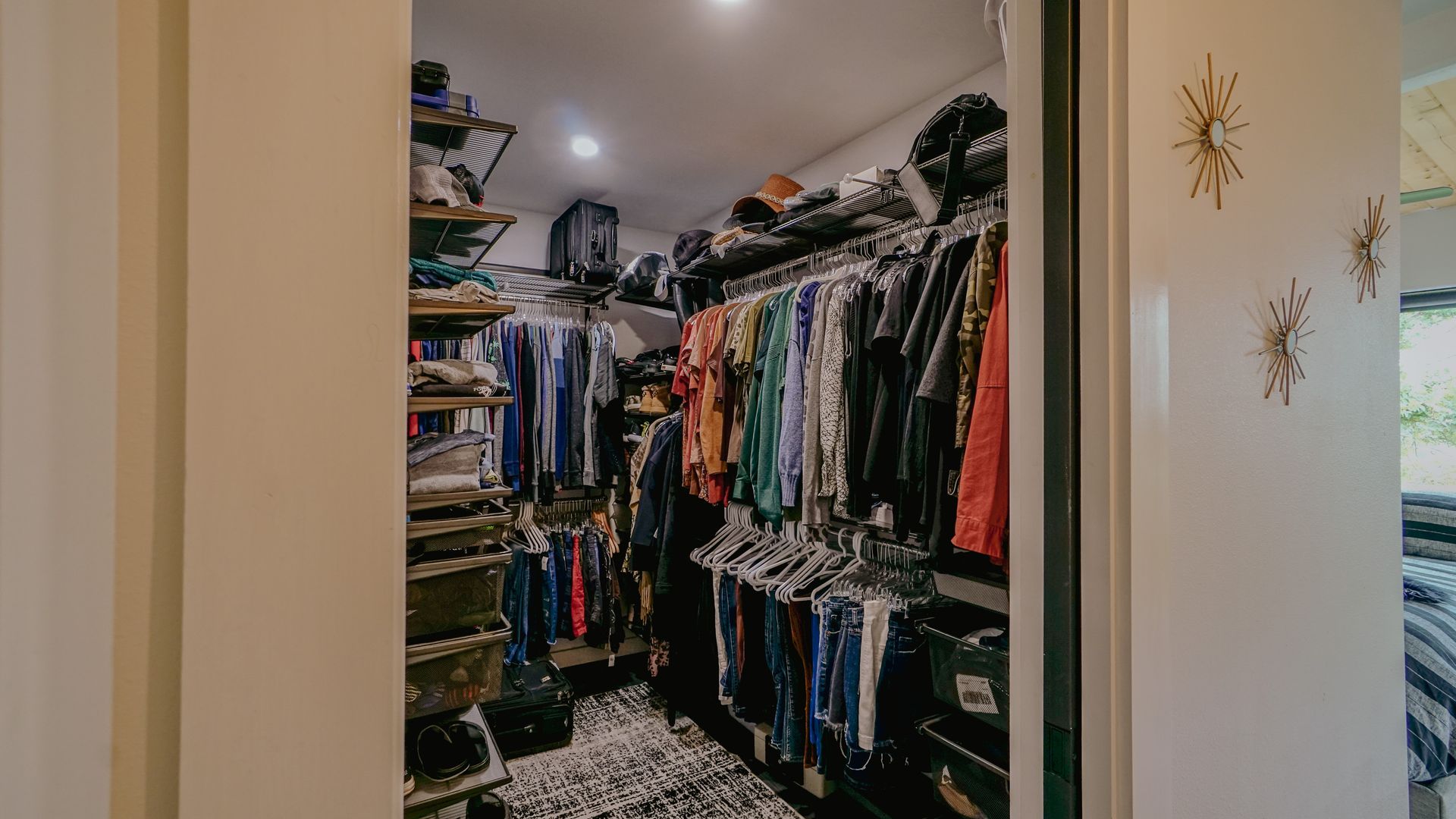 Walk-in closet with clothes hanging on racks, shelves holding shoes, and a patterned rug.