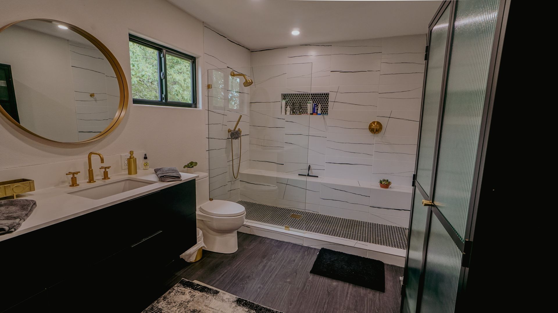 Modern bathroom with a round mirror, black vanity, and white tiled shower with glass door.