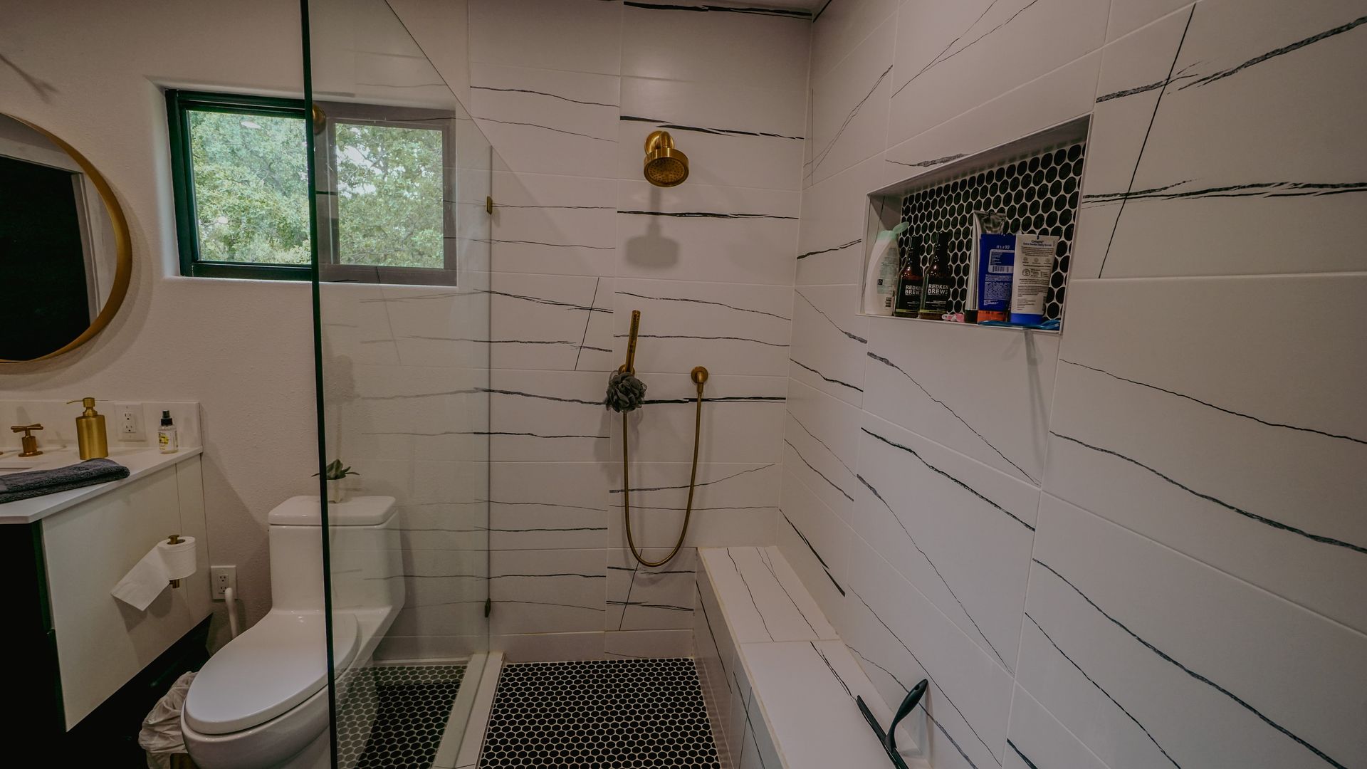 Modern bathroom with white and black striped tile, glass shower, and gold fixtures.