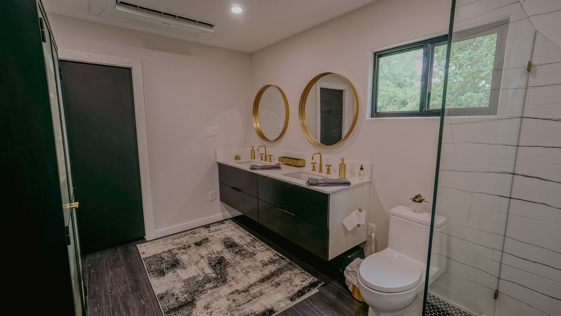 Bathroom with a black vanity, gold-framed mirrors, and a patterned rug.