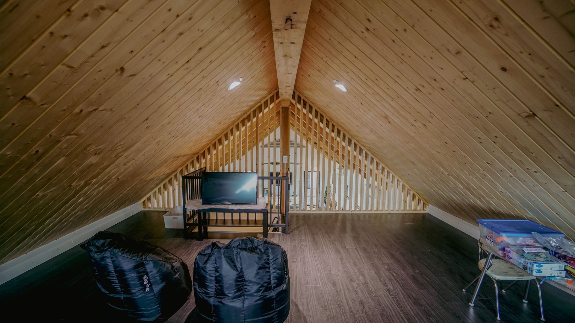 Interior view of an unfinished attic space. Wood paneling on walls and ceiling, dark flooring, two bean bag chairs.
