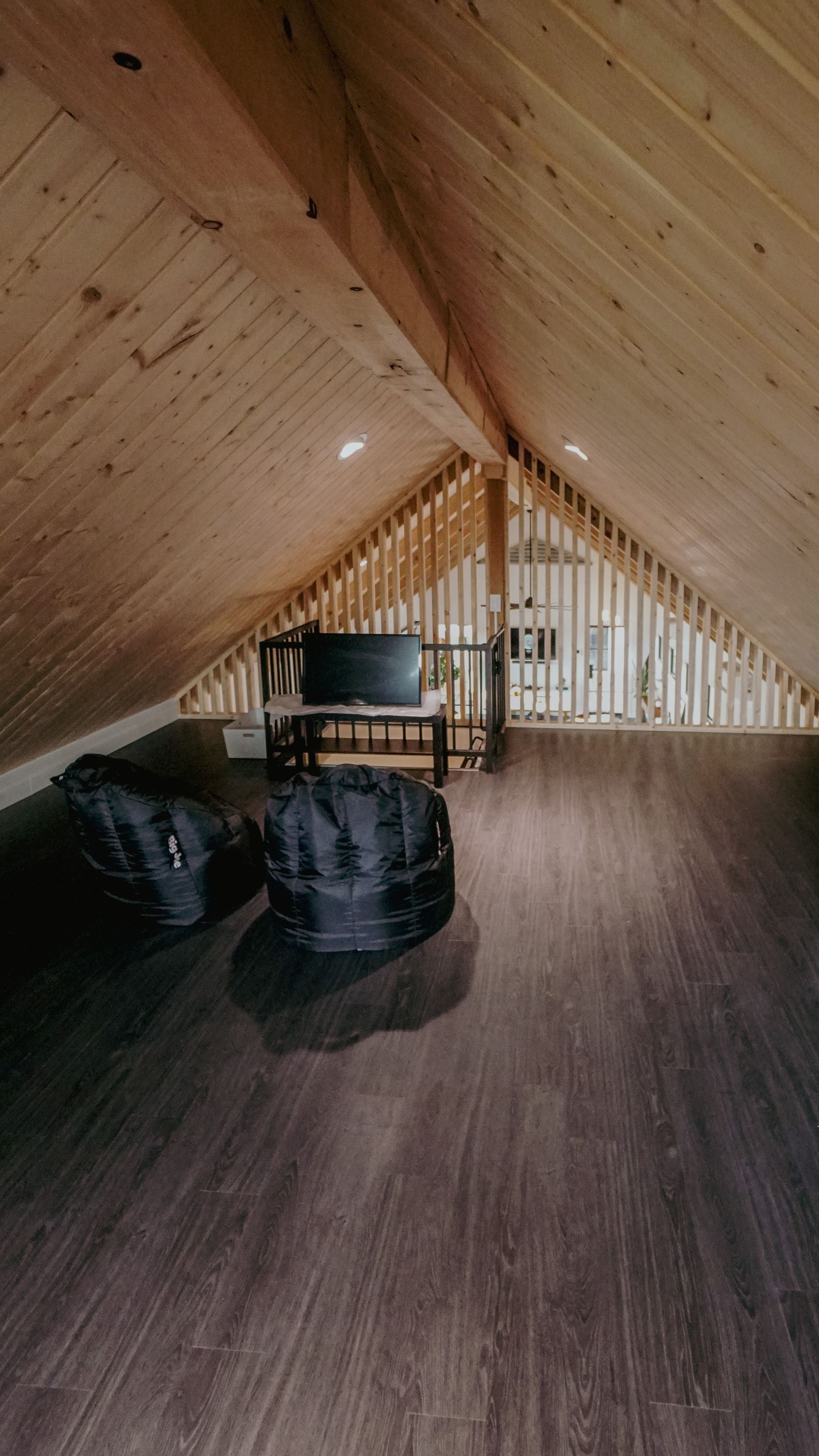 Loft with wood paneling, dark flooring, and two beanbag chairs. A desk and the side of a staircase are in the background.