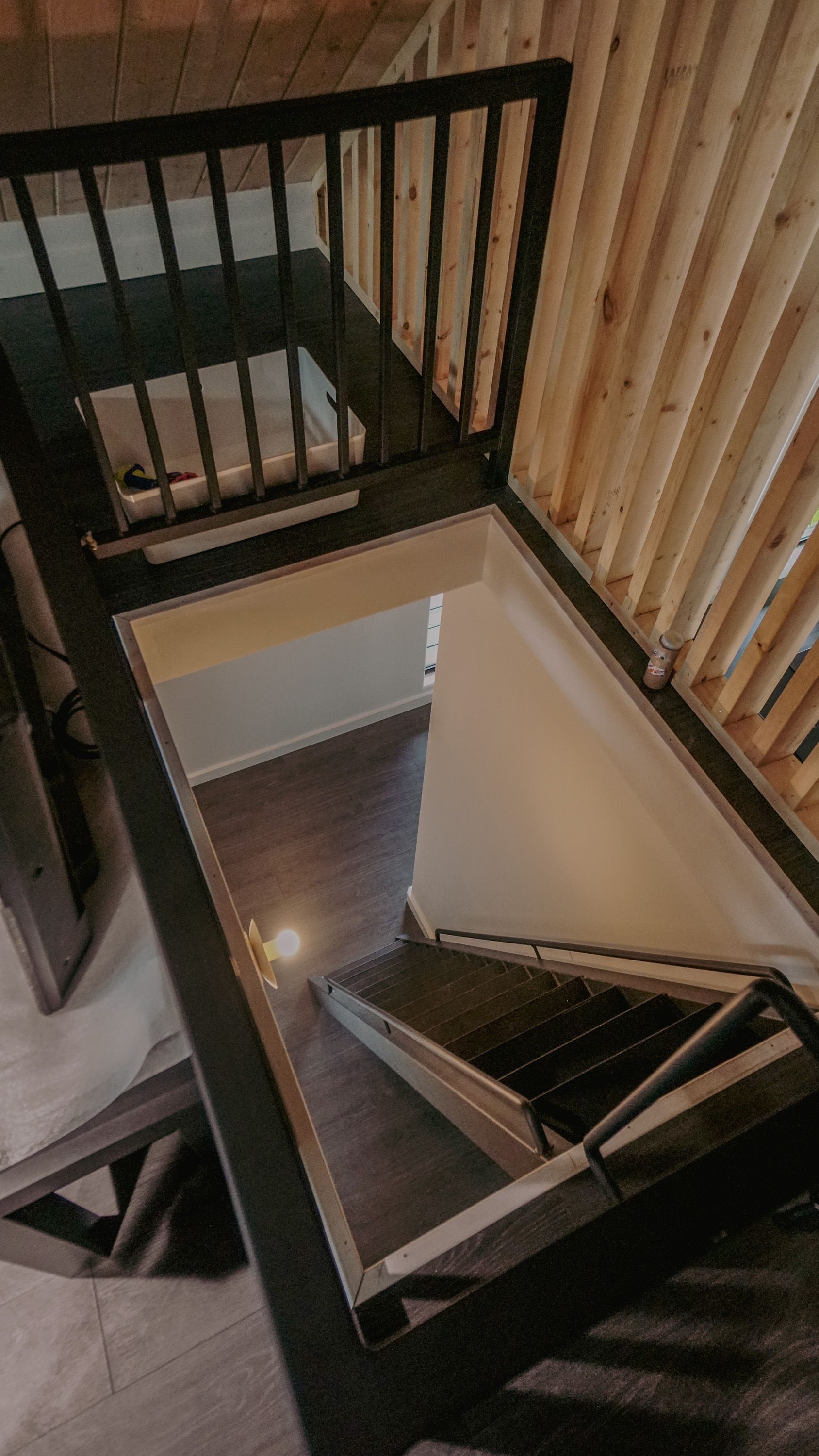 Wooden-framed stairs leading down, viewed from above, with black handrail and wood paneling on the right.