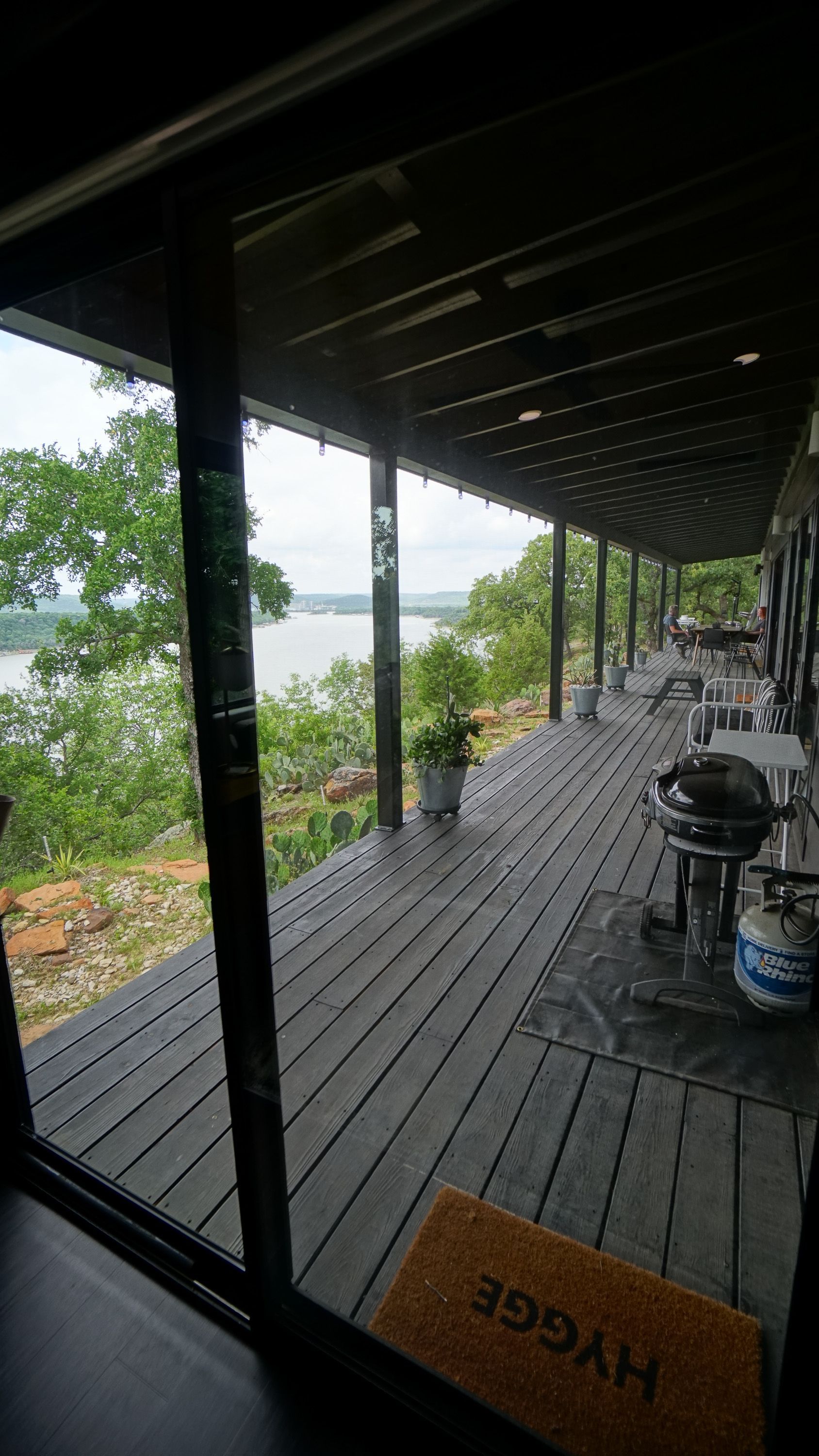 View from a covered porch overlooking a lake, with grilling equipment and a 