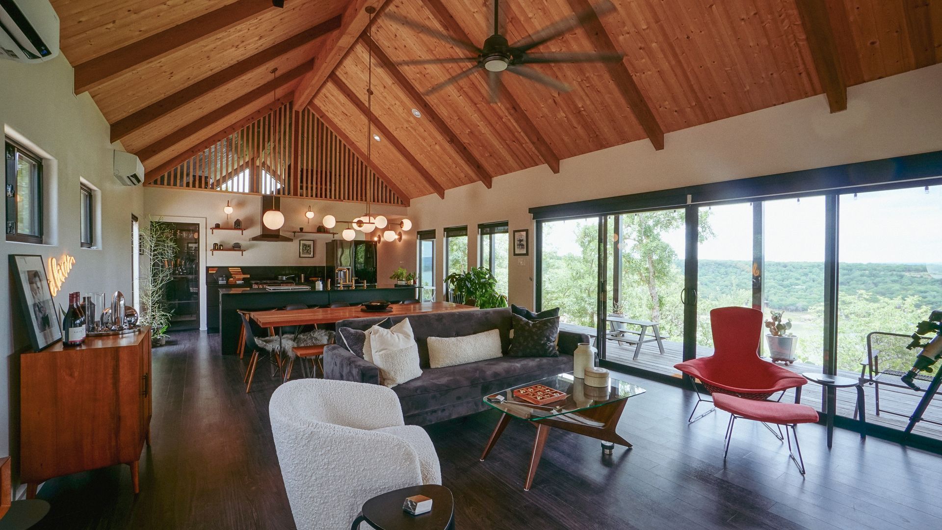 Spacious living room with vaulted wood ceiling, open to kitchen and large windows overlooking a scenic vista.