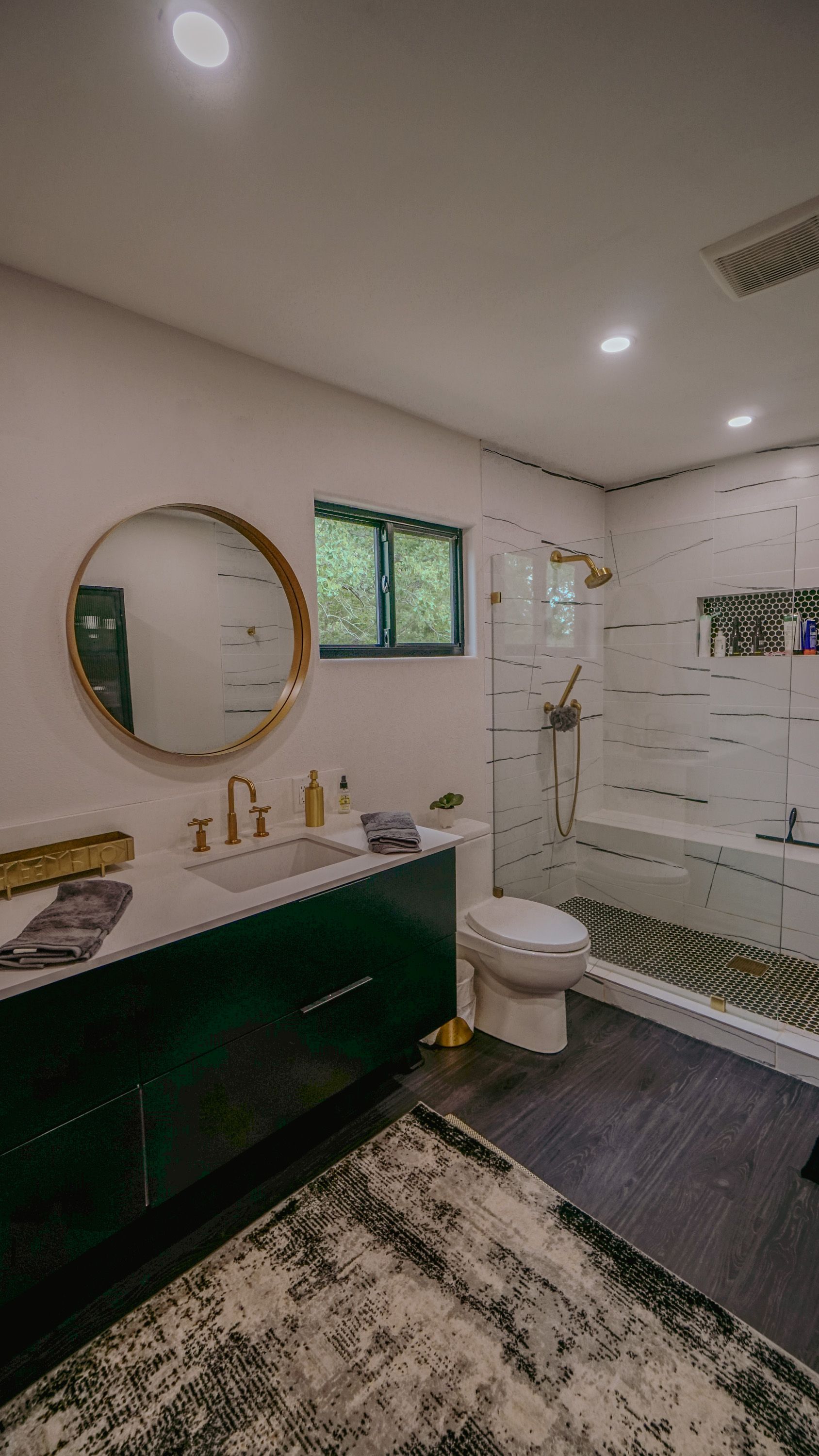 Green and white modern bathroom with gold accents, circular mirror, and dark flooring.