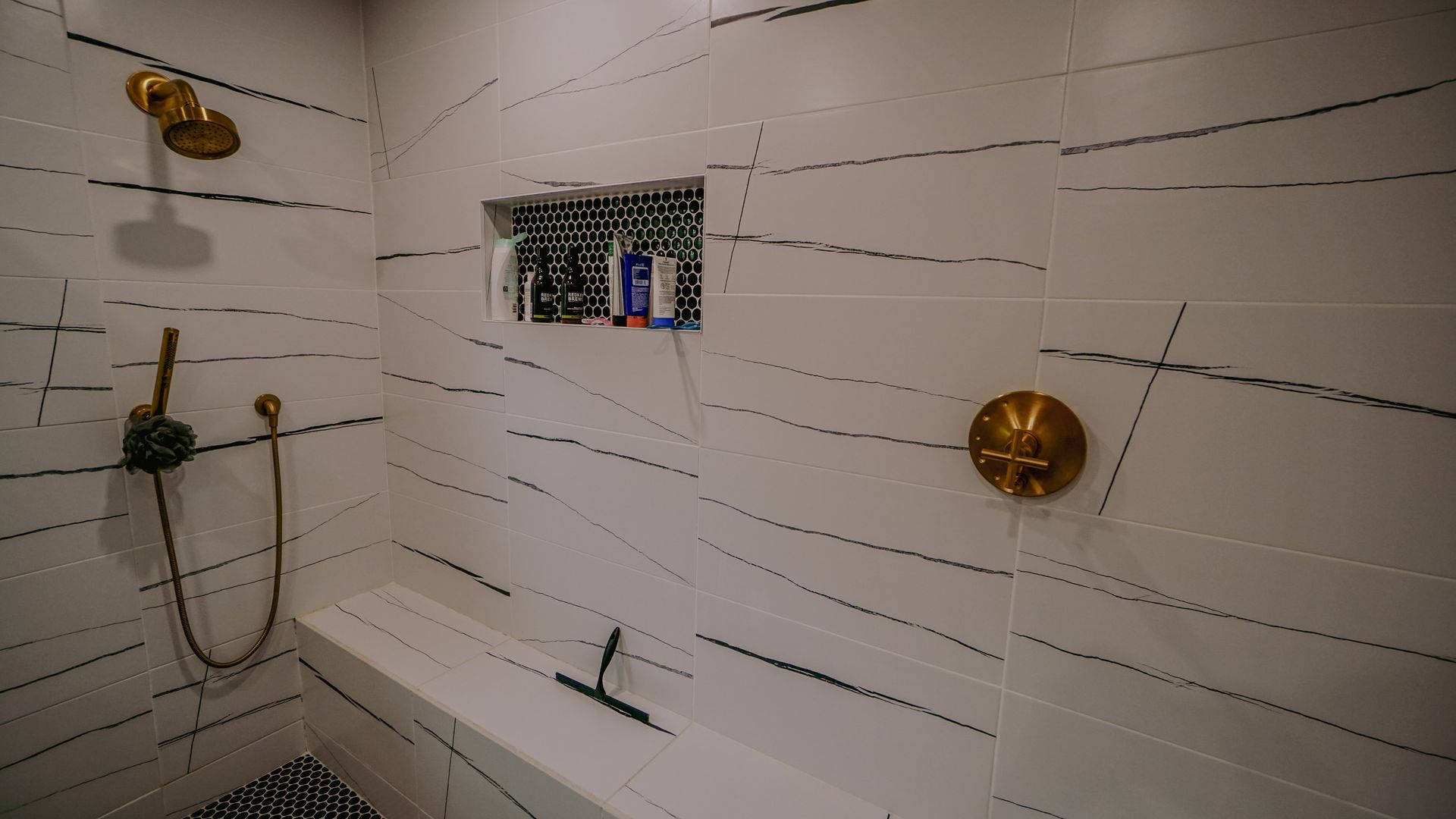White tiled shower with black line details, gold fixtures, and built-in shelf.