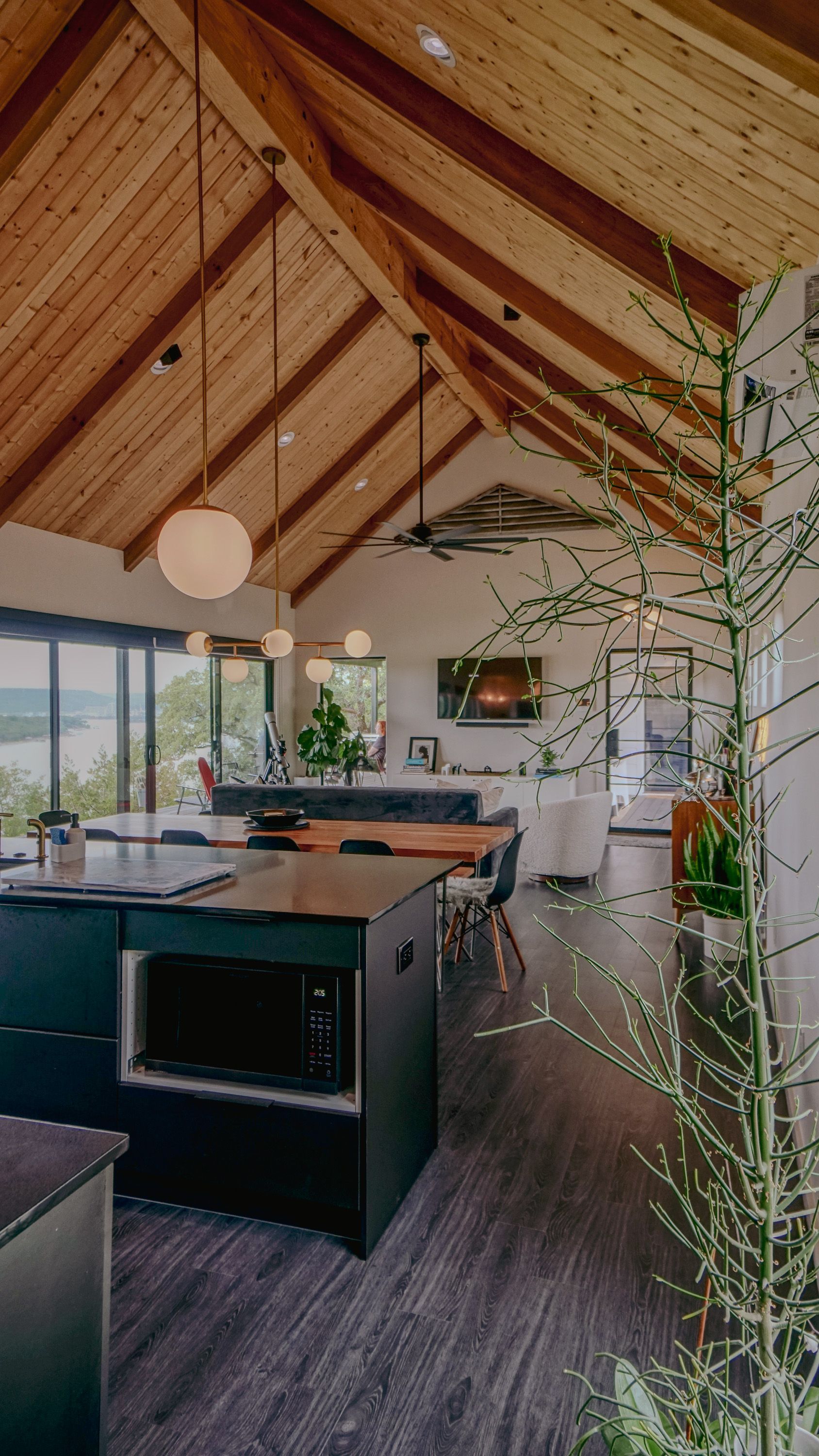 Modern kitchen with wood-beamed ceiling, dark cabinets, island, and large windows overlooking a view.
