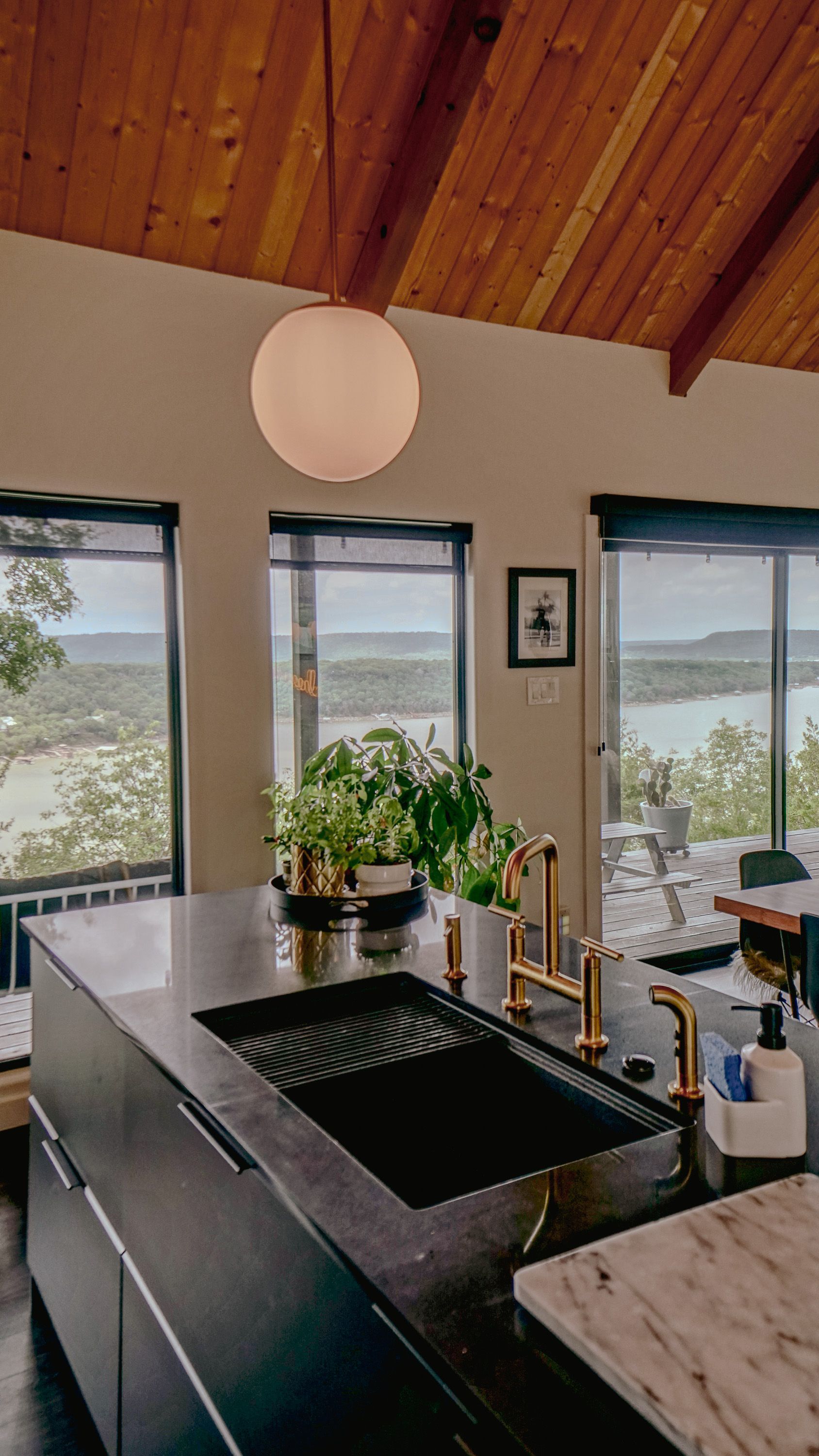 Modern kitchen with black island, gold fixtures, globe light, and scenic view.