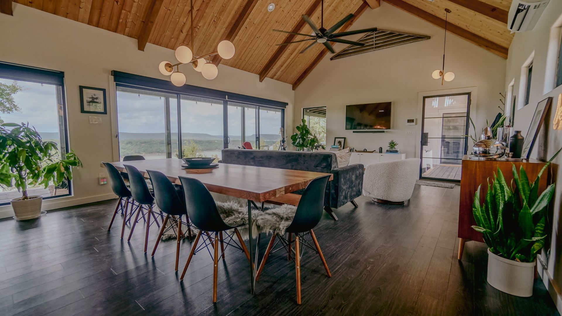 Dining room with wooden table and black chairs, large windows, and a high, wooden ceiling.