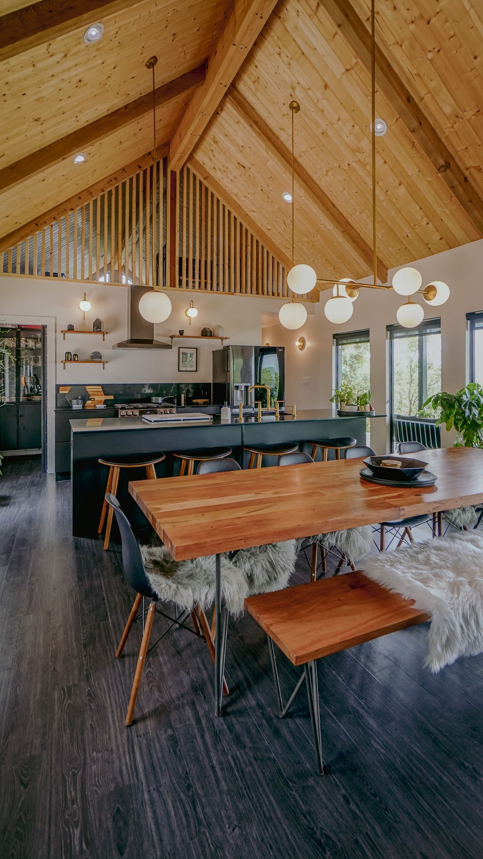 Spacious kitchen with wood ceiling and modern chandelier, dark cabinets, and long wooden dining table.