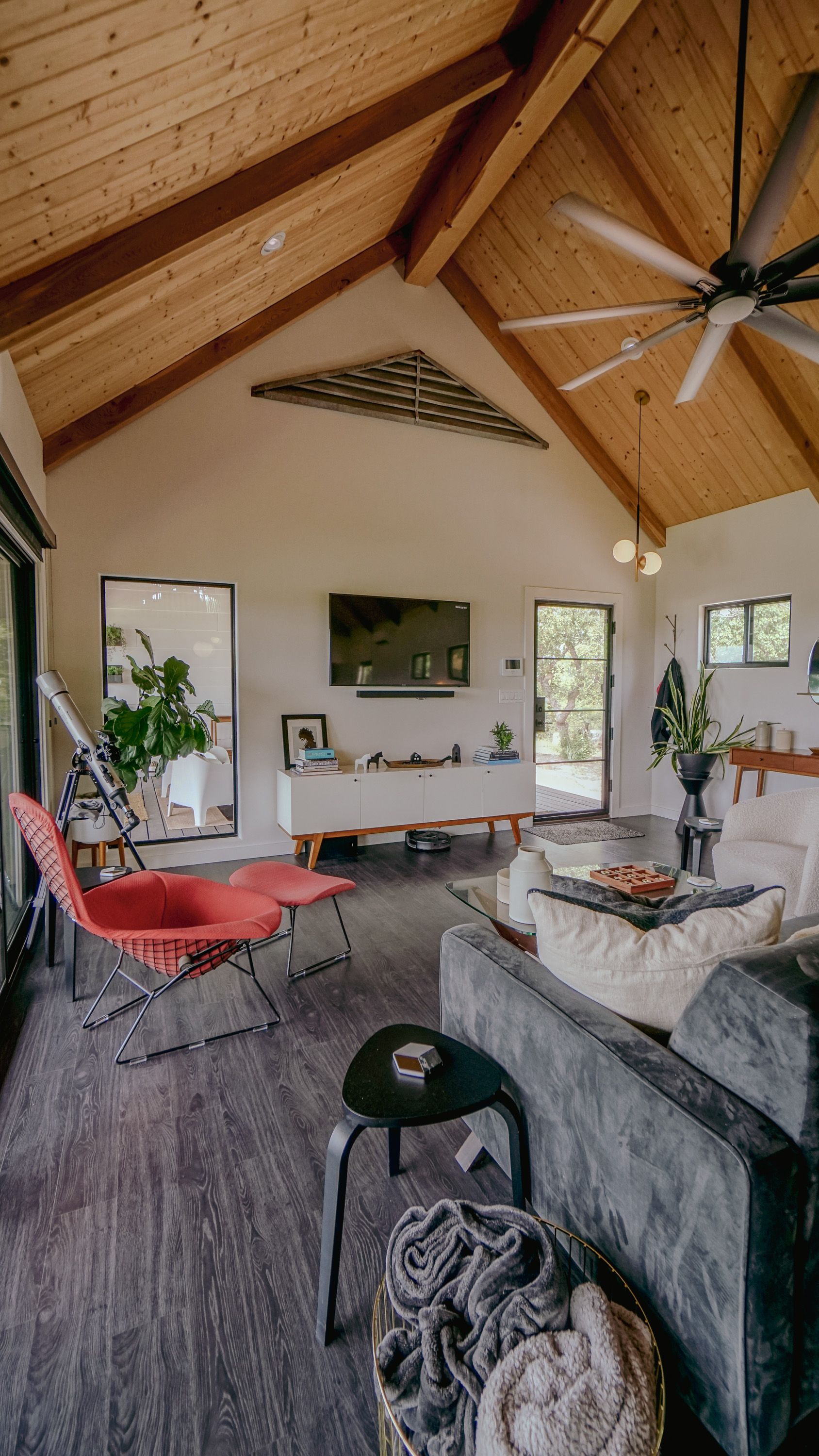 Living room with vaulted wood ceiling, red chair, gray couch, large mirror, and TV.