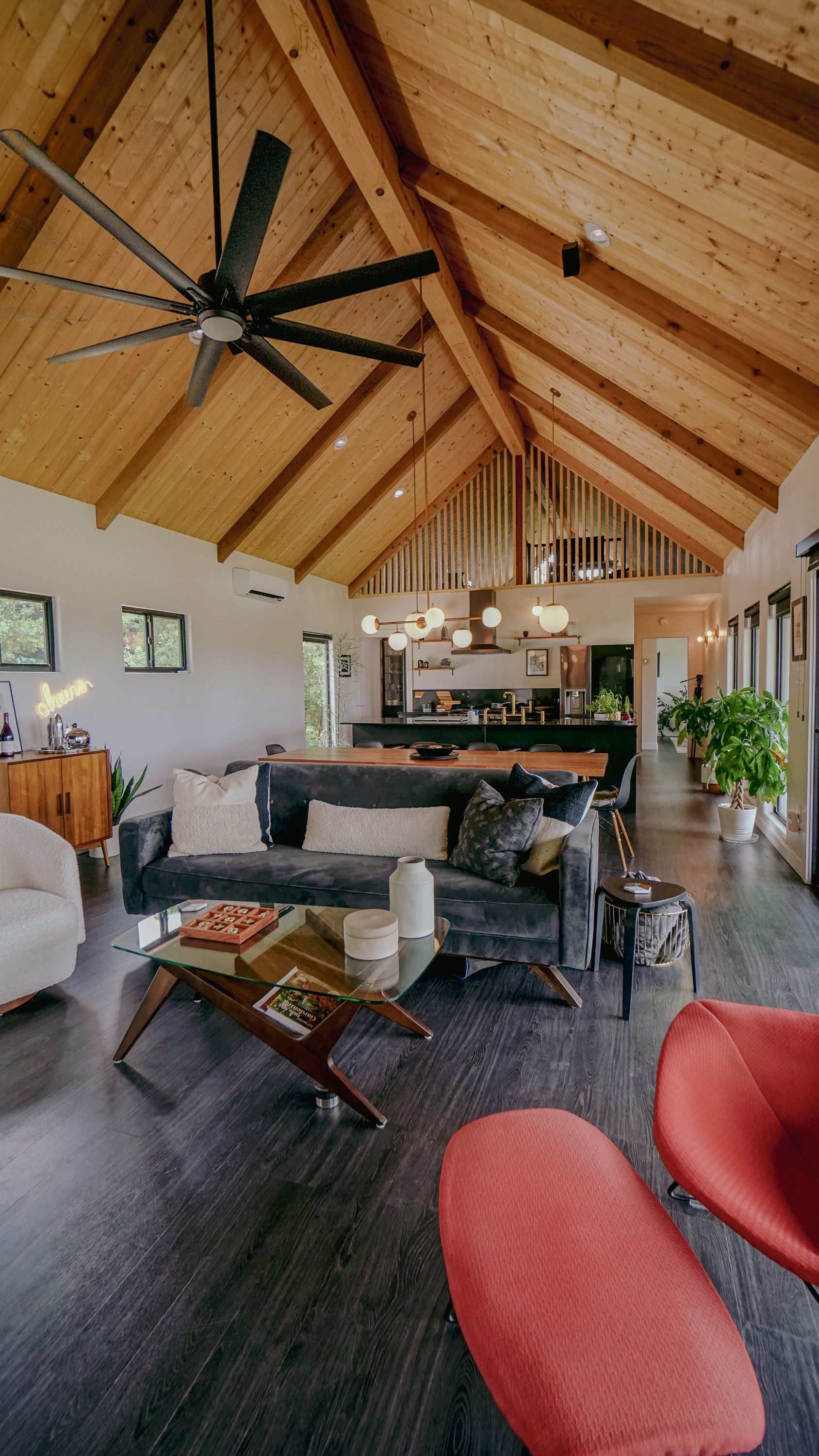 Spacious living room with wood ceiling, dark floors, modern furniture, and a large black fan.