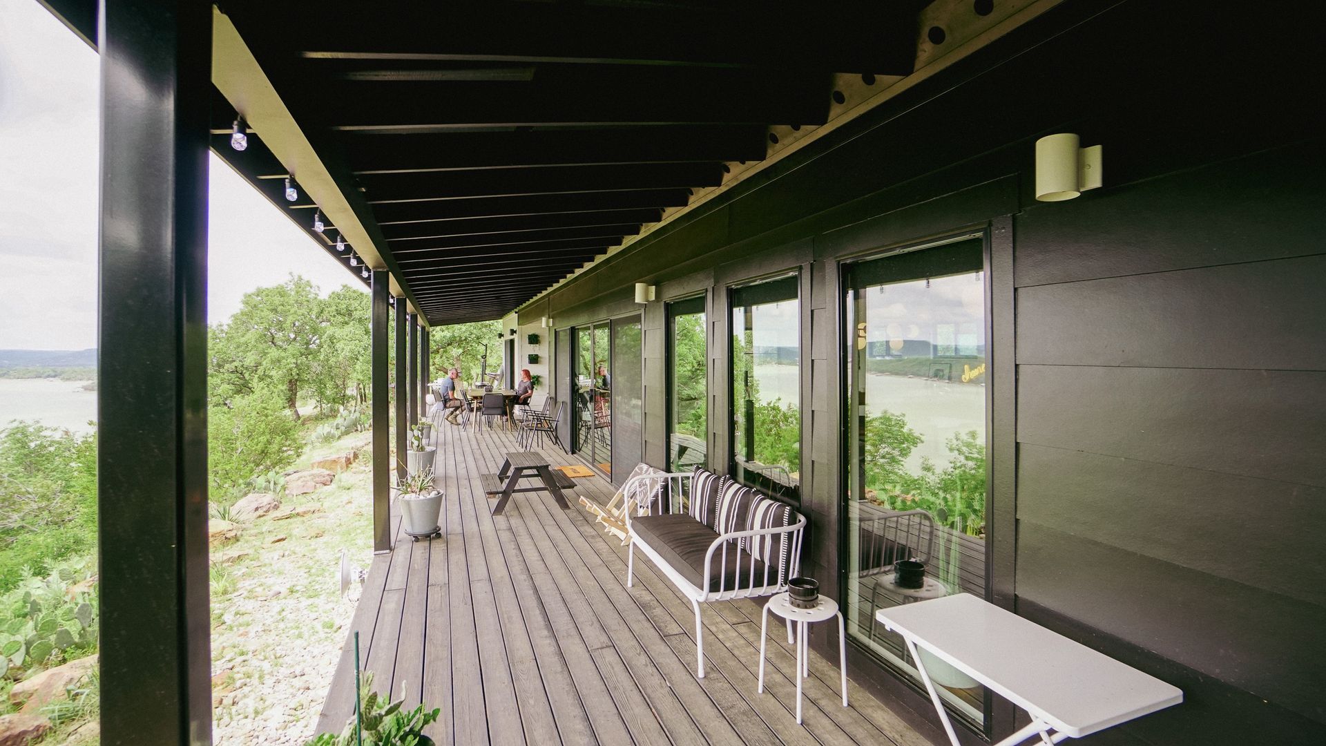 Long wooden porch with black exterior, overlooking a scenic landscape with trees and water.