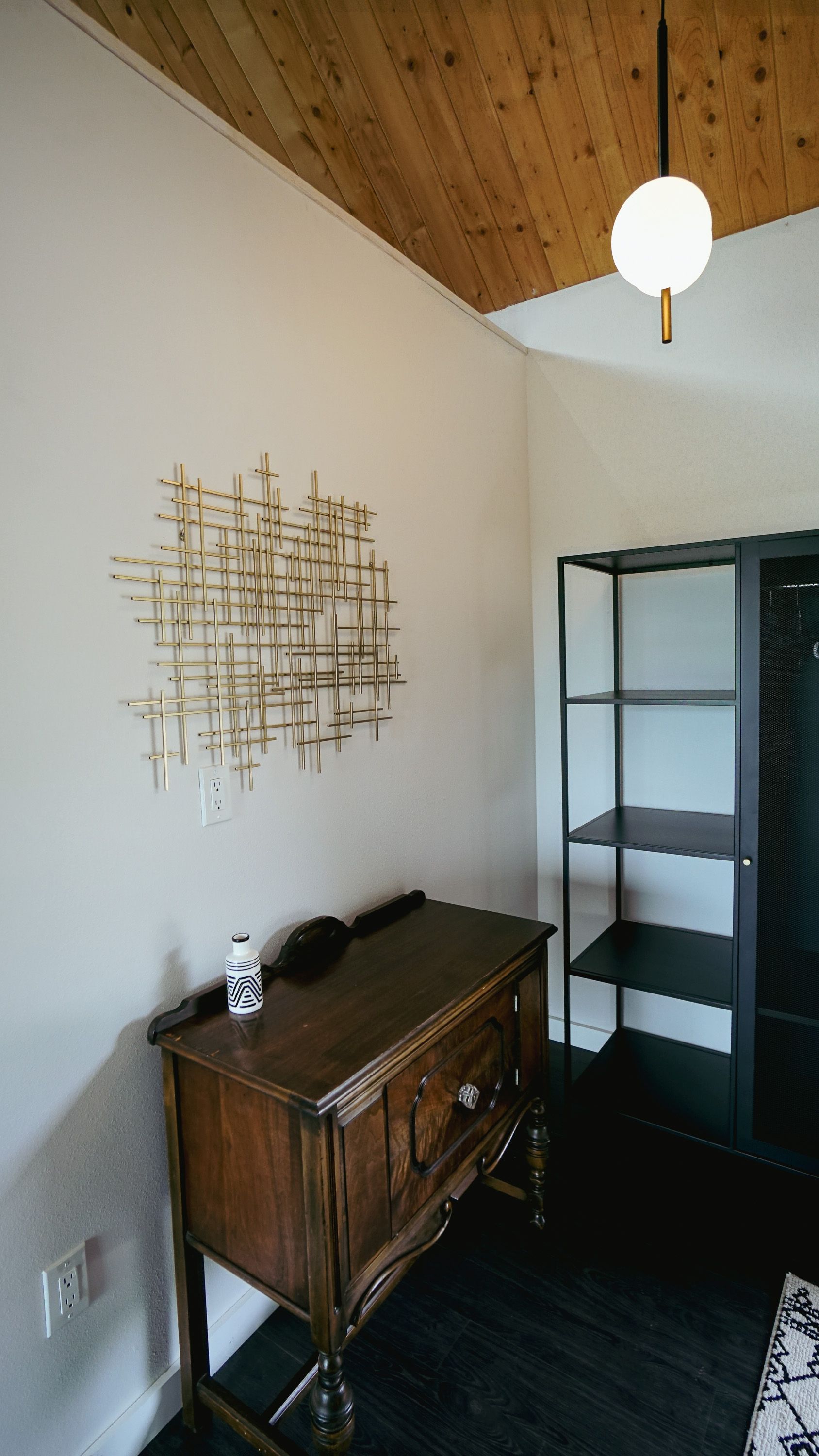 Wooden desk with art and shelving in a room with a wood ceiling and black floor.