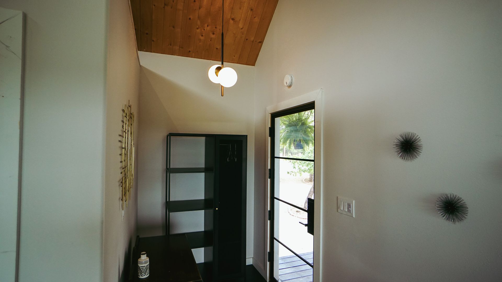 Entryway with a black door, shelving unit, and a wooden ceiling.