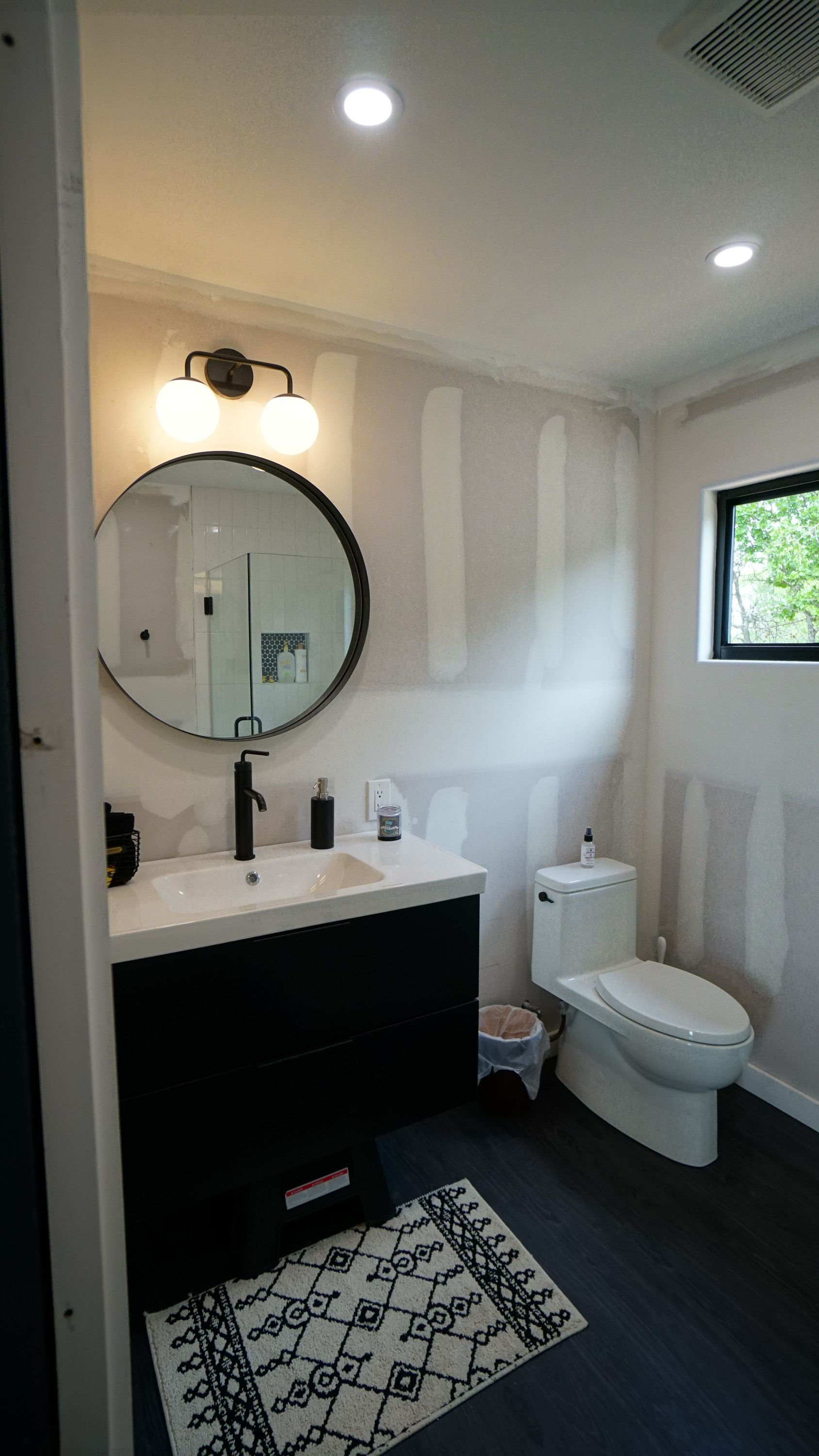 Bathroom with black vanity, round mirror, striped walls, and a toilet.