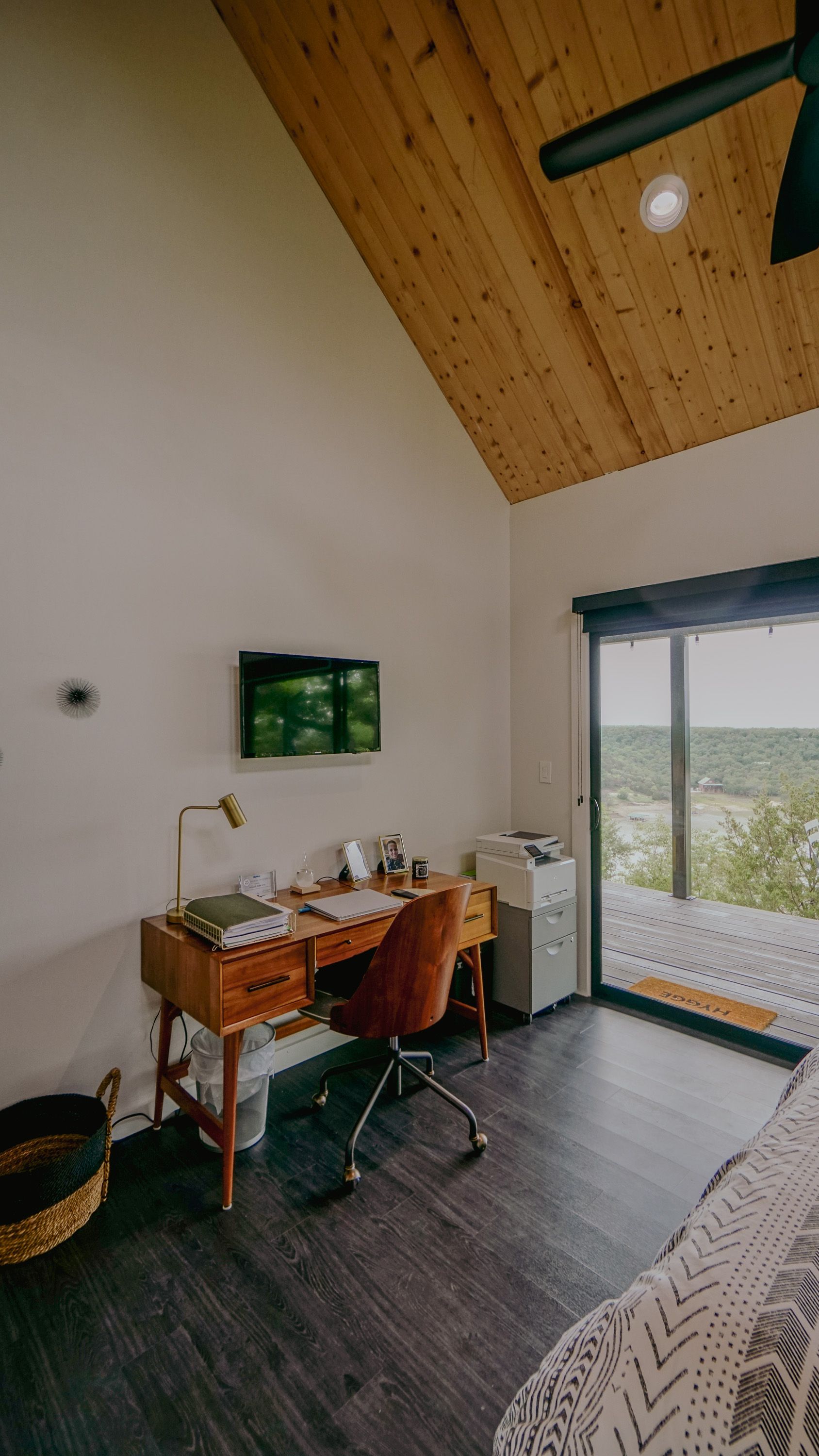 A home office with a desk, chair, and TV; a sliding glass door leads to an outdoor view.