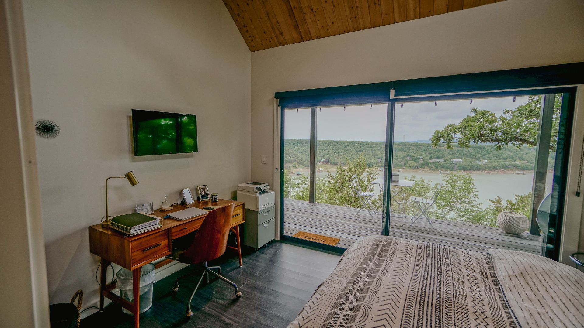 Bedroom with desk, TV, and large window overlooking a lake.