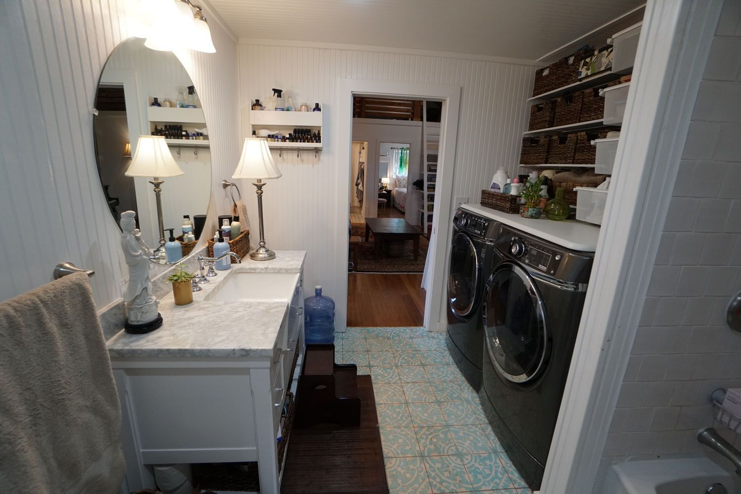 Bathroom with a vanity, washer/dryer, and shelves with baskets; a doorway leads to another room.
