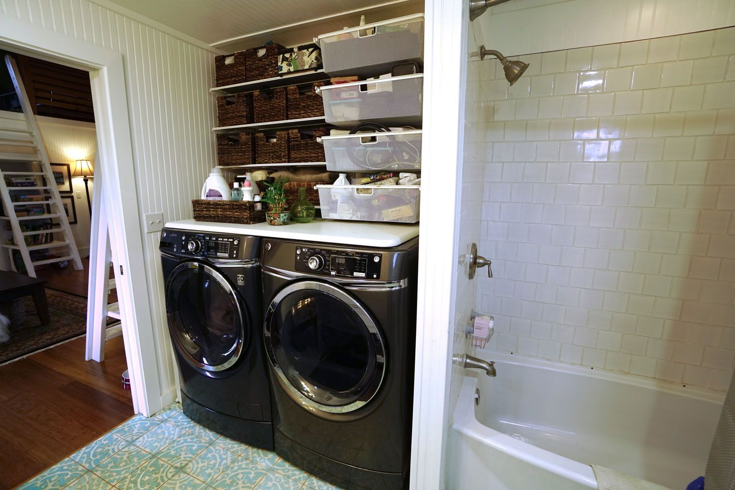 Laundry machines next to a bathroom with shelving and storage.