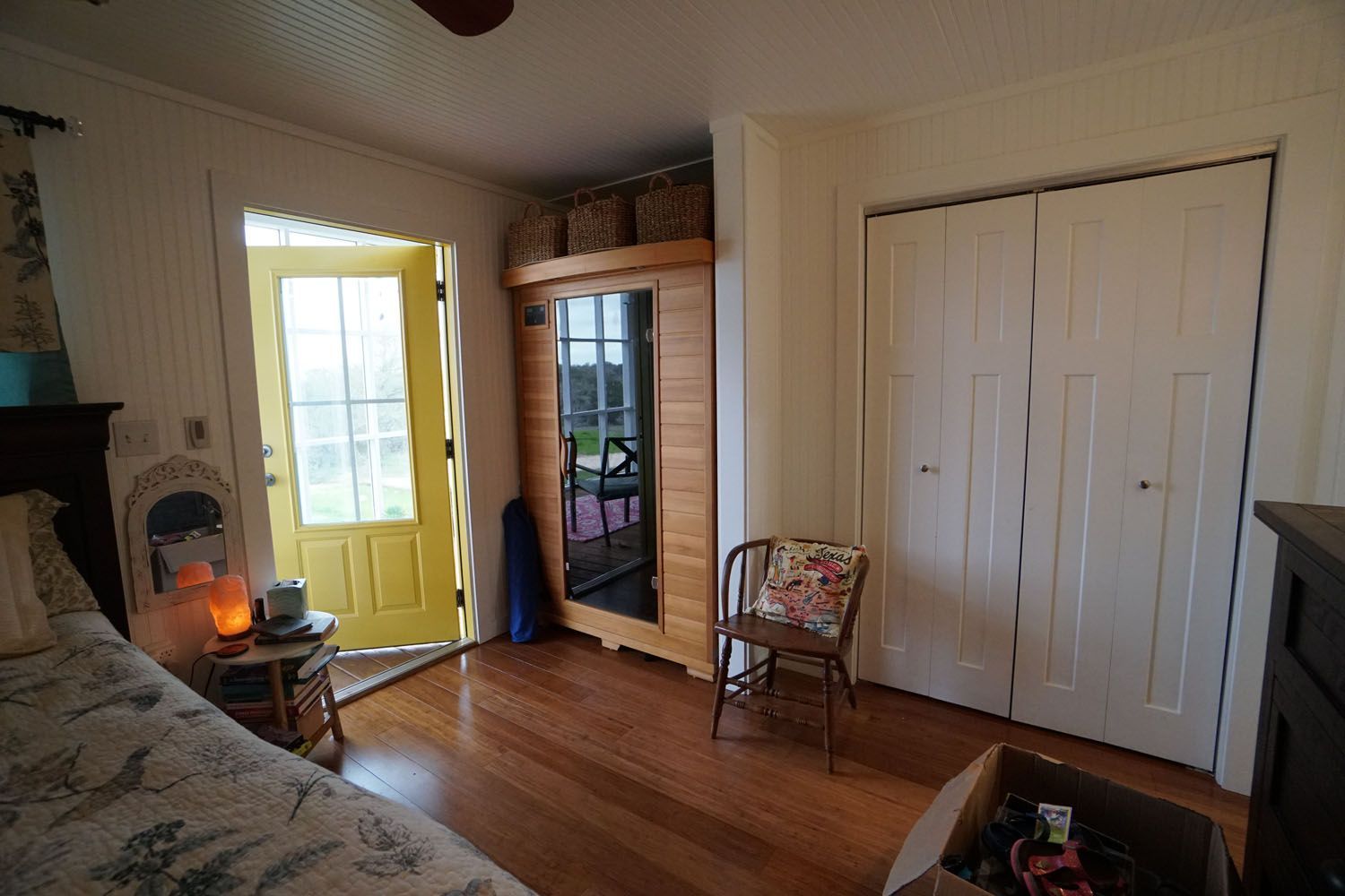 Bedroom with wooden floors, open yellow door, sauna, closet, and chair.