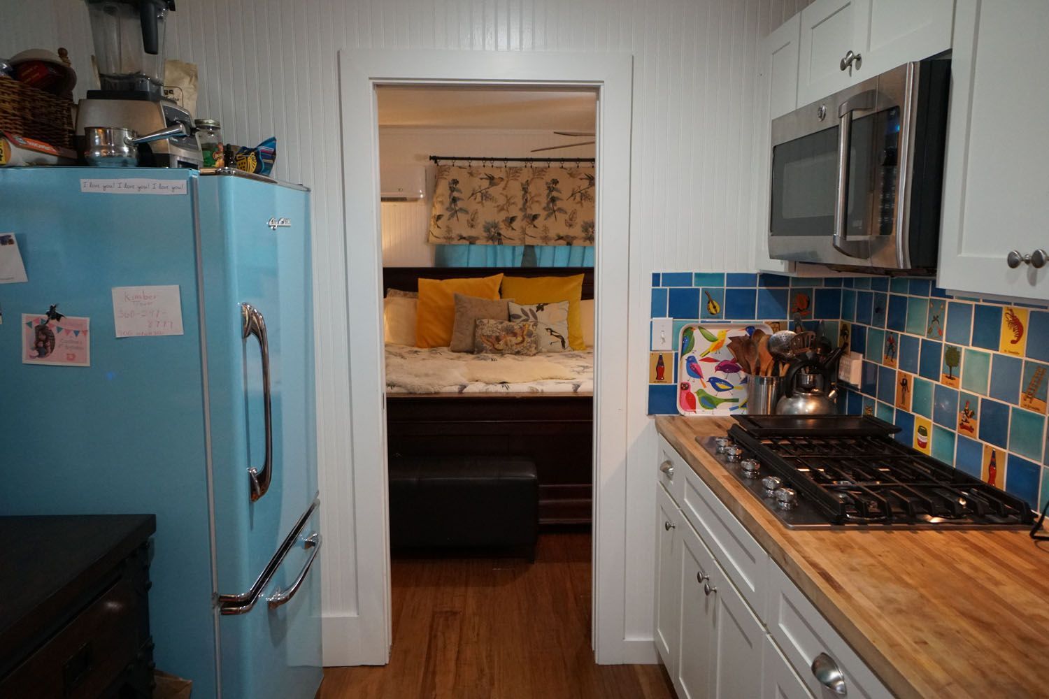 Kitchen doorway leads to a bedroom. Blue fridge on the left, stovetop and microwave on the right.