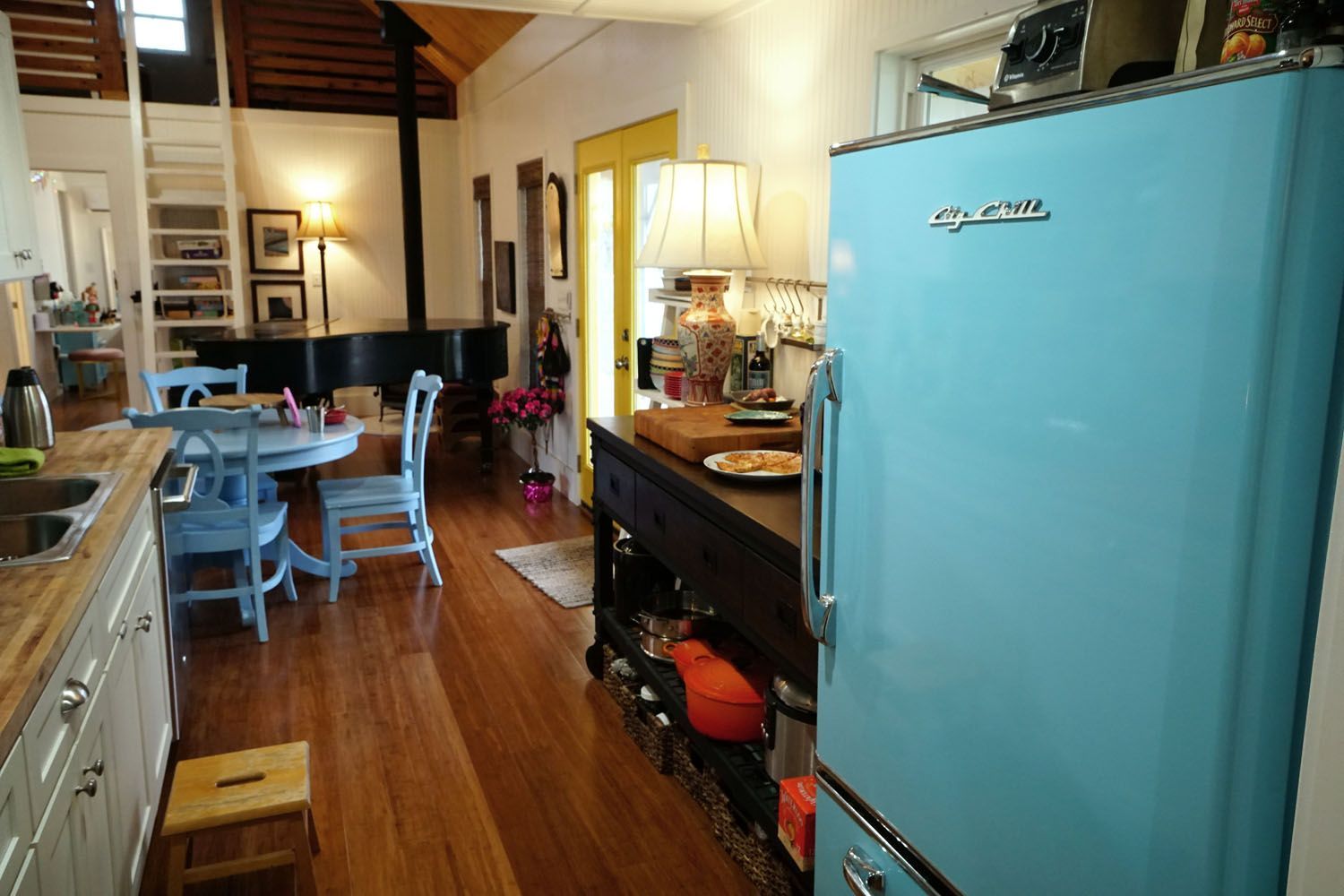 Light blue retro refrigerator in a kitchen with hardwood floors, leading to a dining area.