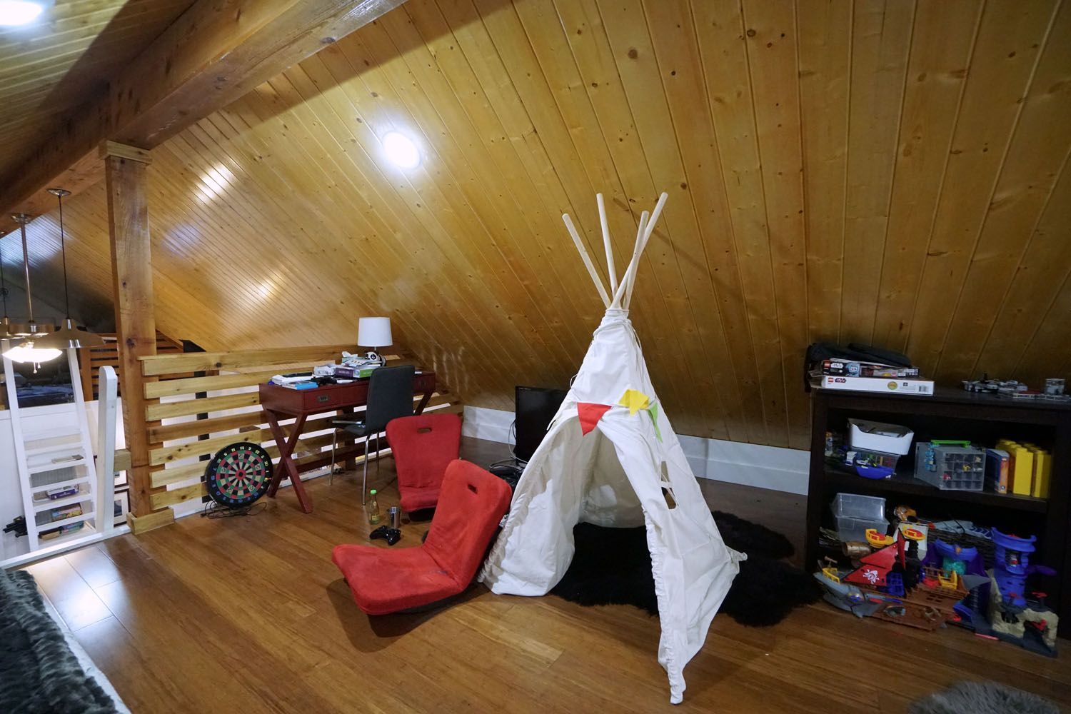 Playroom with teepee, red chairs, desk, and shelves in a wood-paneled attic space.