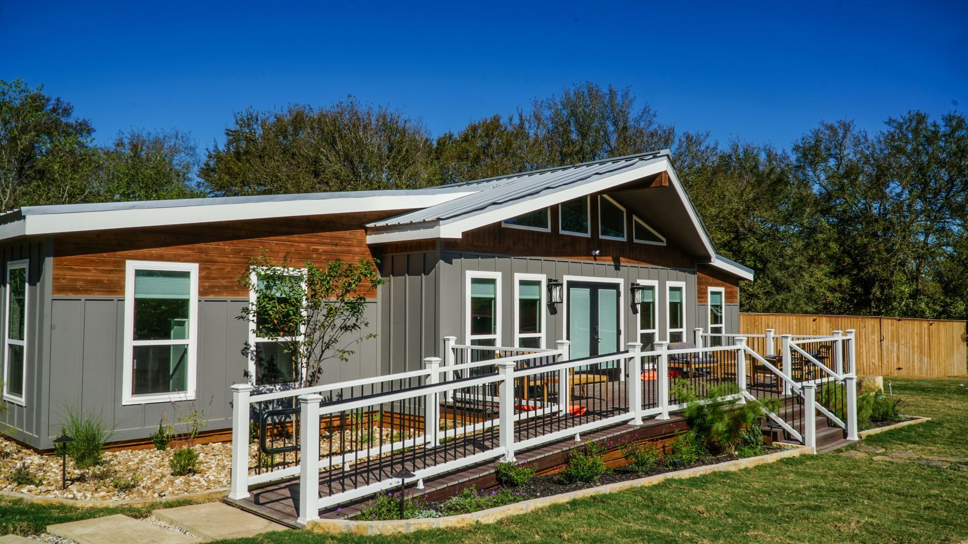Gray and brown house with a ramp and railing for accessibility. Sunny, outdoor setting.