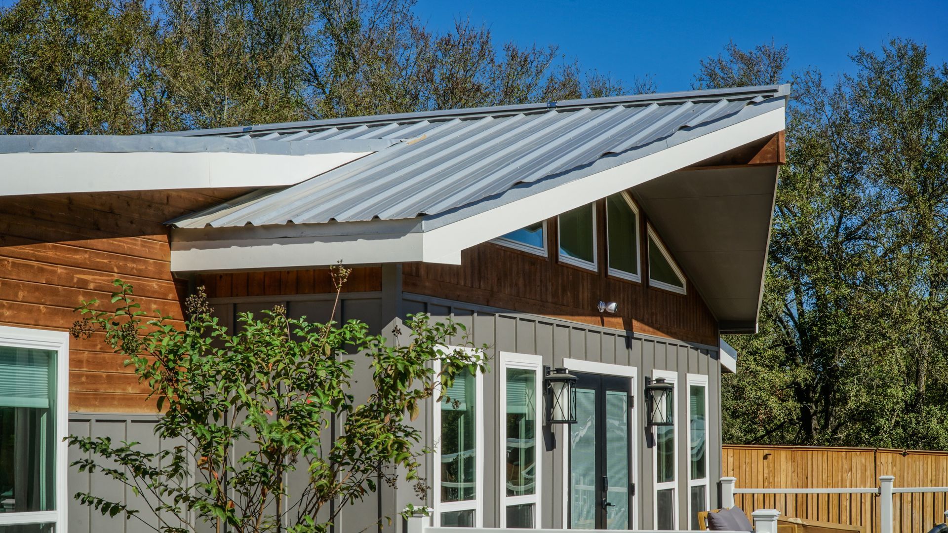 Modern house with a sloped metal roof, wood siding, and large windows on a sunny day.