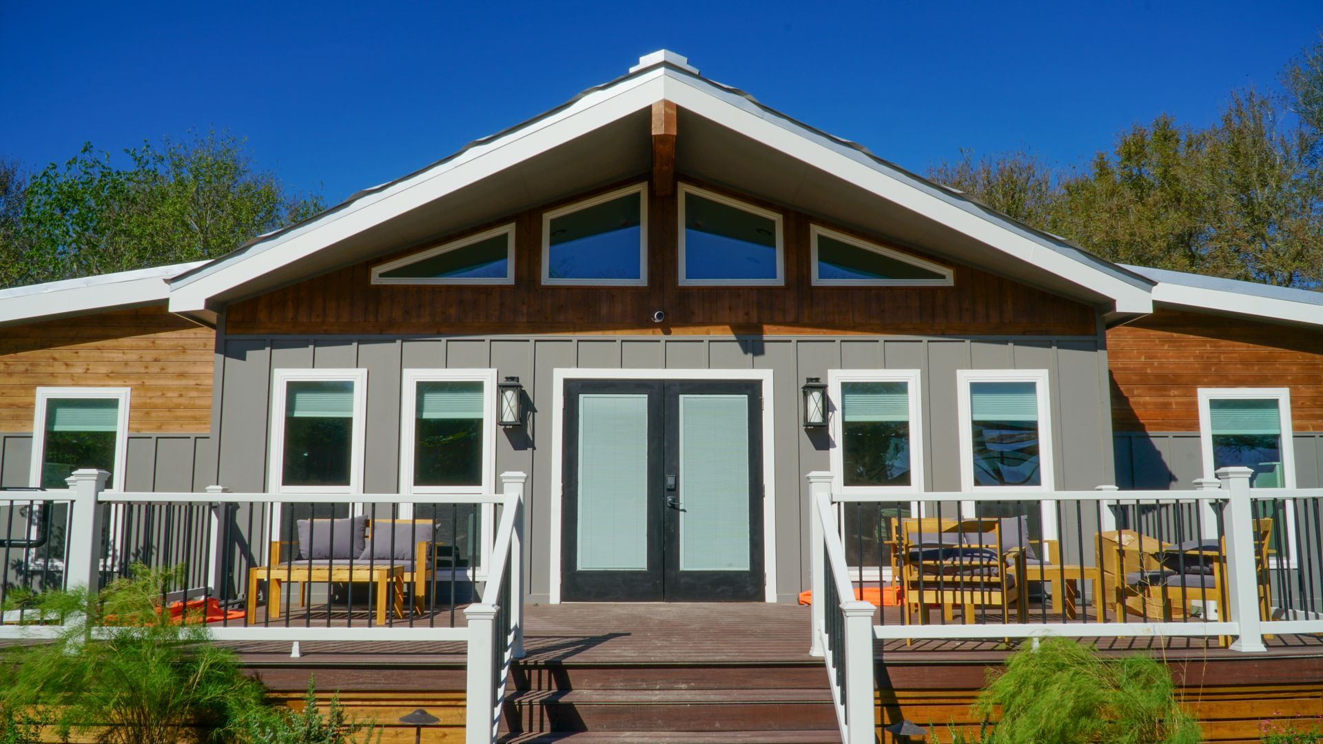 Gray house with a wooden deck and steps, double doors, and angled windows.