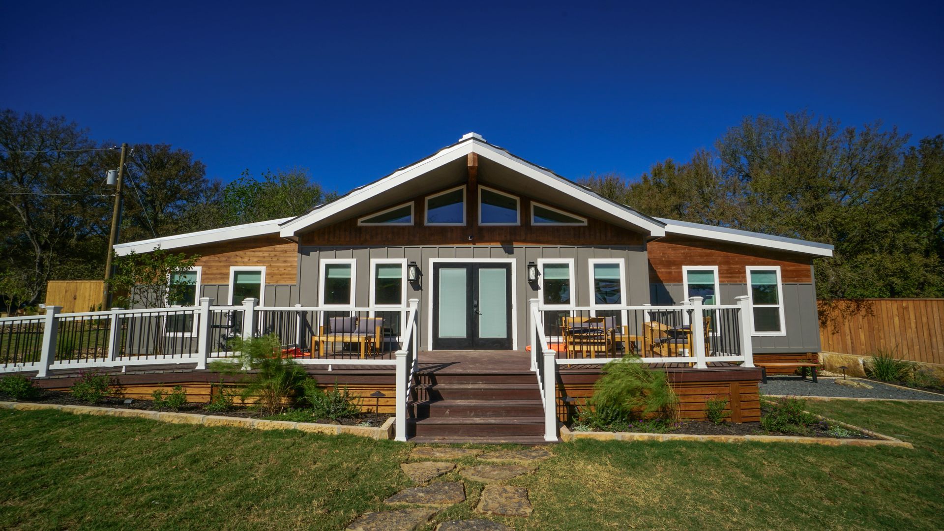 A single-story house with gray siding, a brown deck, and a blue sky.