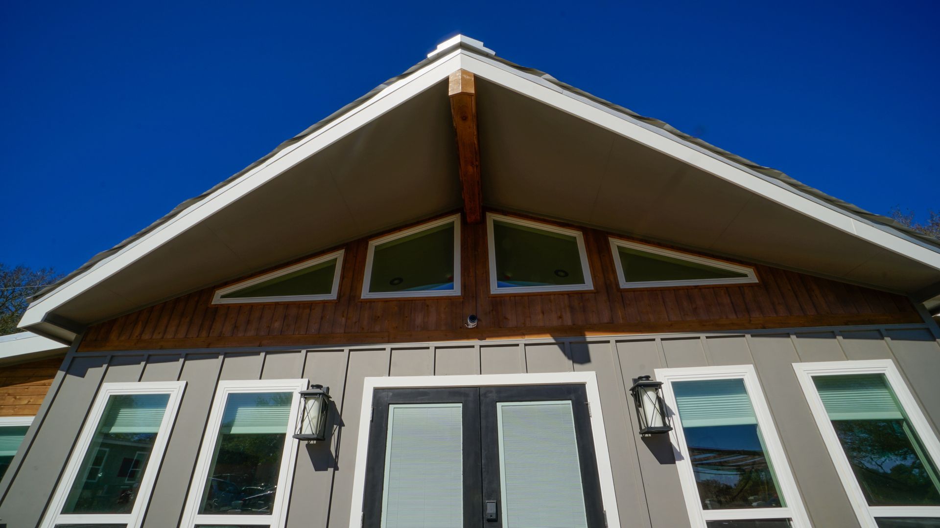 Modern home exterior with gray siding, triangular roof, and multiple windows against a blue sky.