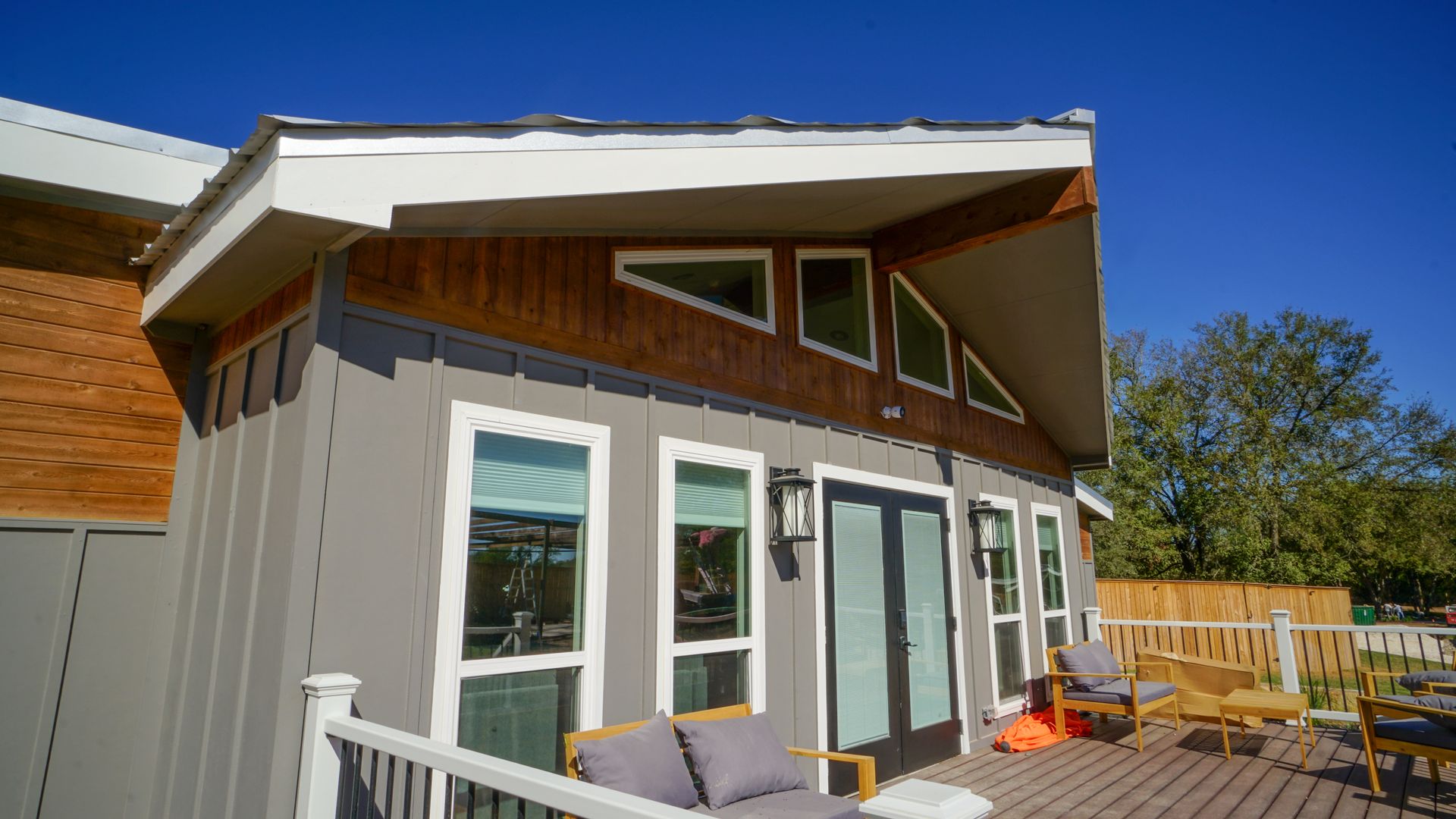 Modern home exterior with gray siding, wood accents, and a deck under a blue sky.
