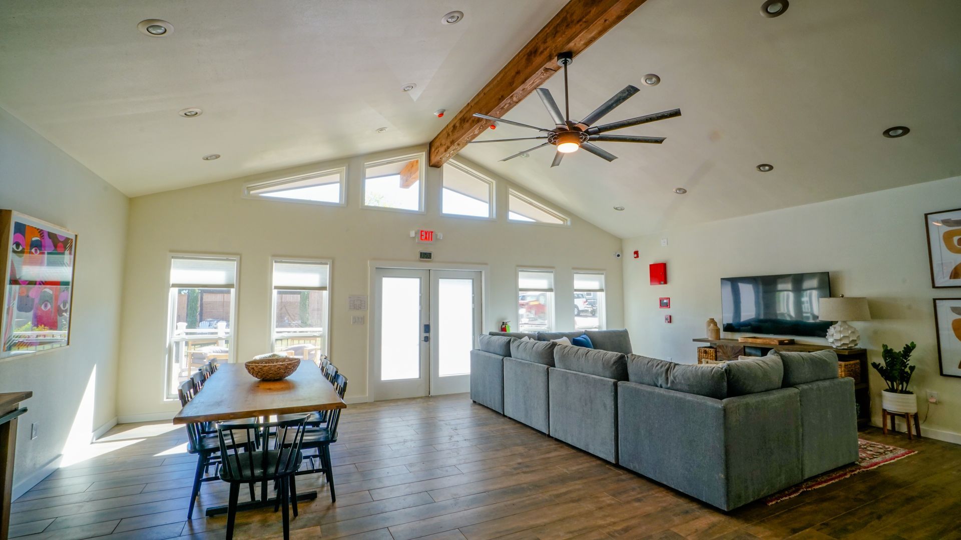 Open living space with sectional sofa, dining table, exposed beams, and high windows.