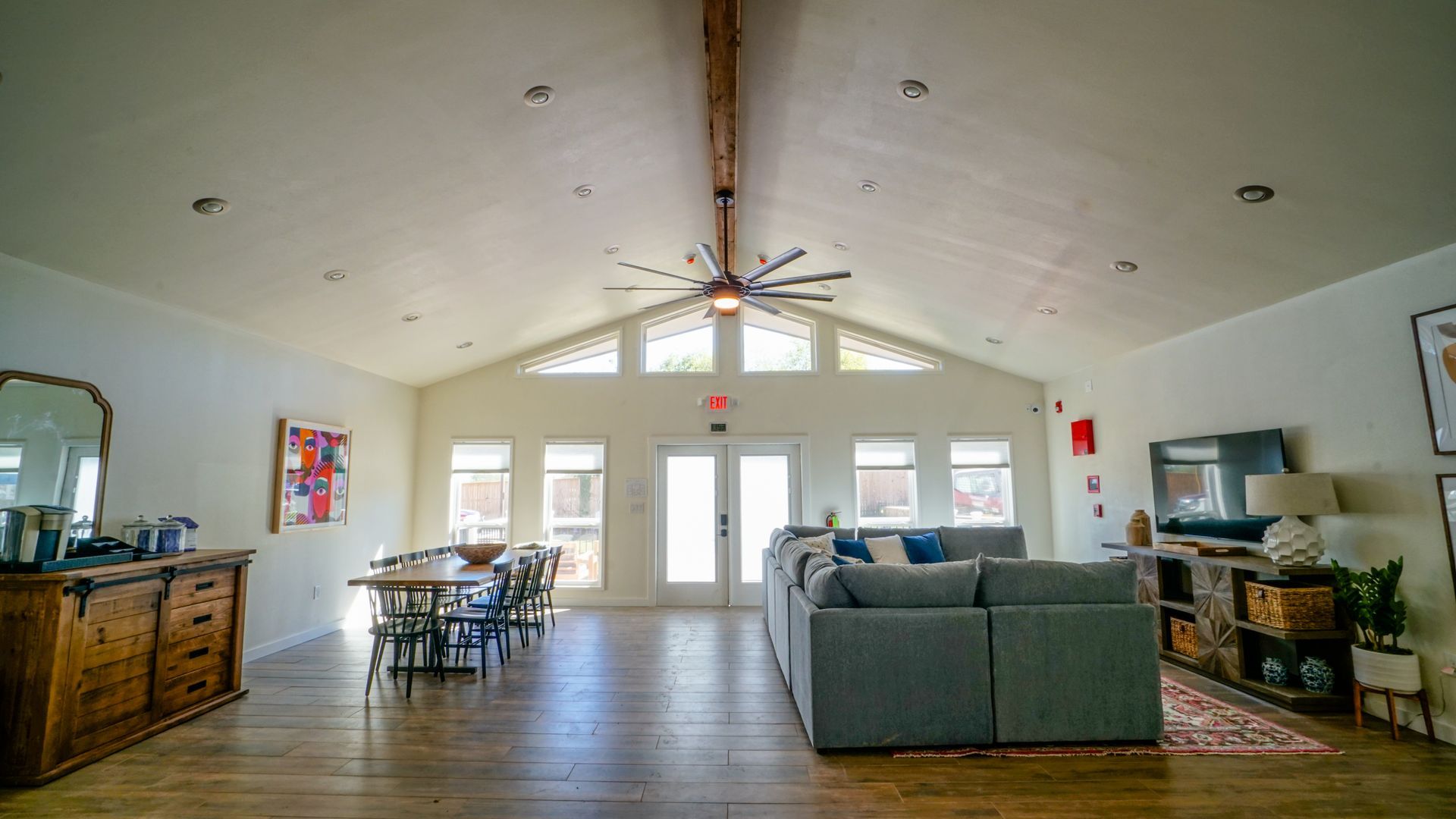 Spacious living room with vaulted ceiling, wood floor, and large windows. Includes seating, dining table, and TV.
