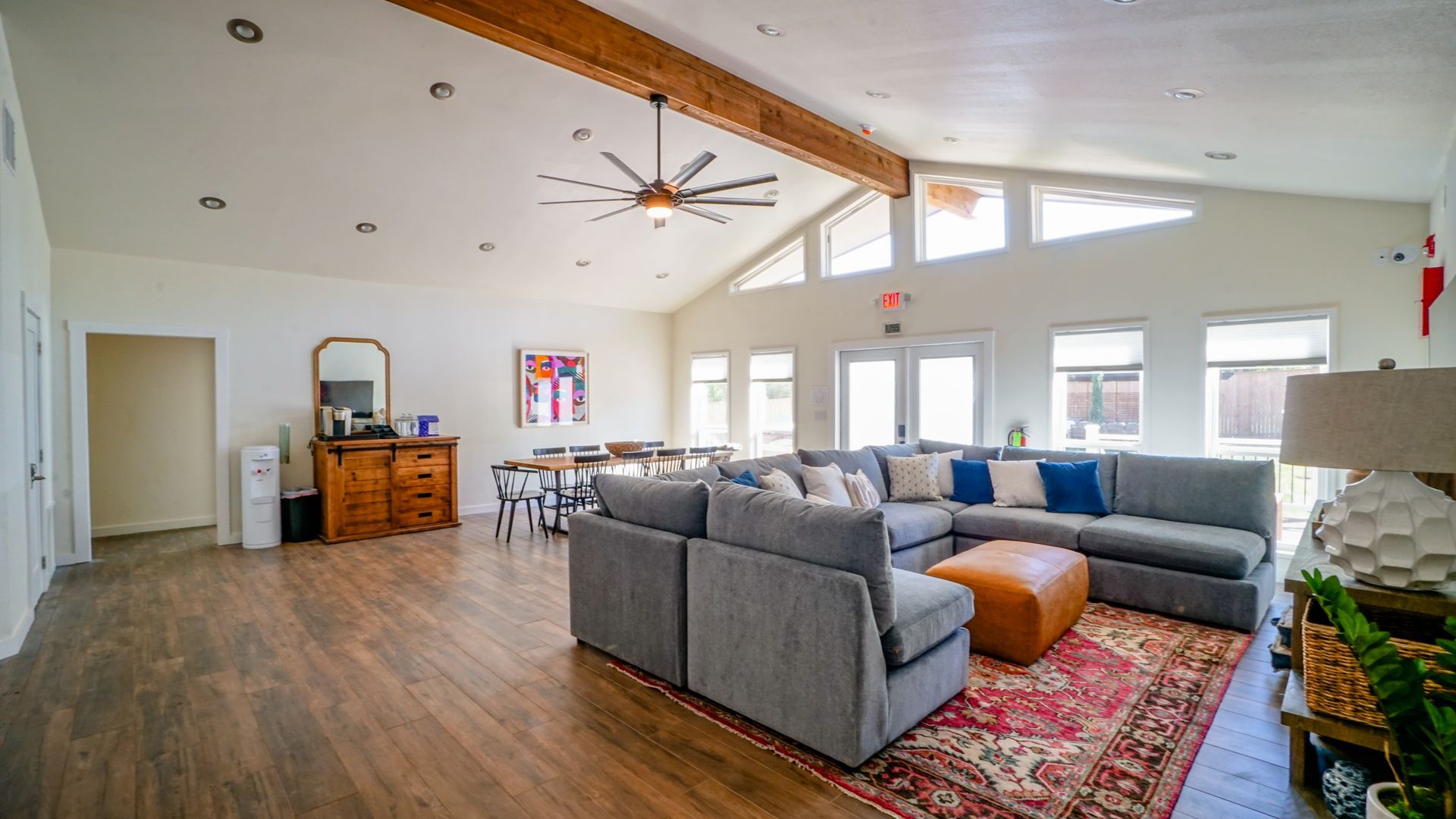 Spacious, well-lit living room with sectional sofa, rug, and tables. Wooden beams and large windows.
