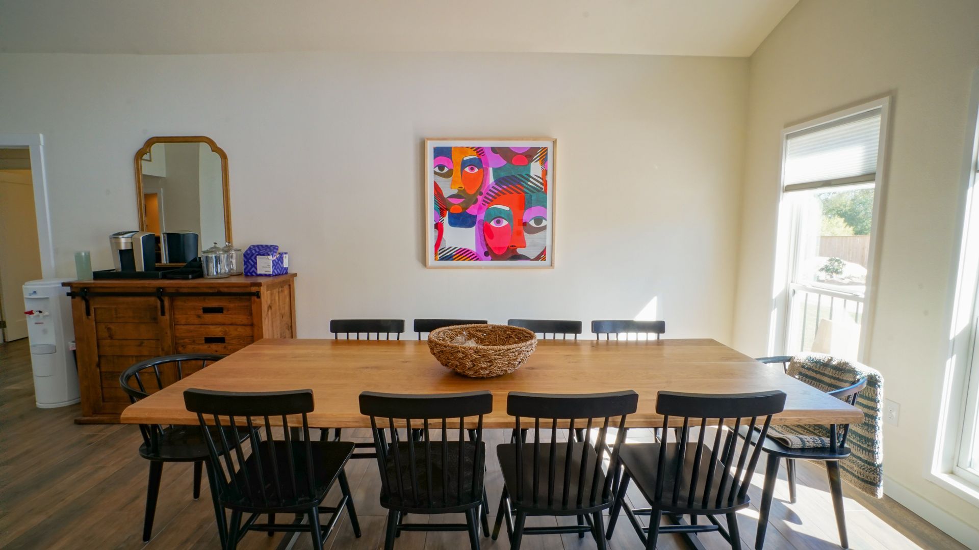 Dining room with large wooden table, black chairs, artwork, and natural light from a window.