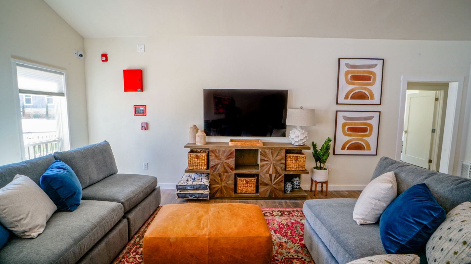 Living room with gray sofas, a wooden TV stand, and abstract art on white walls.