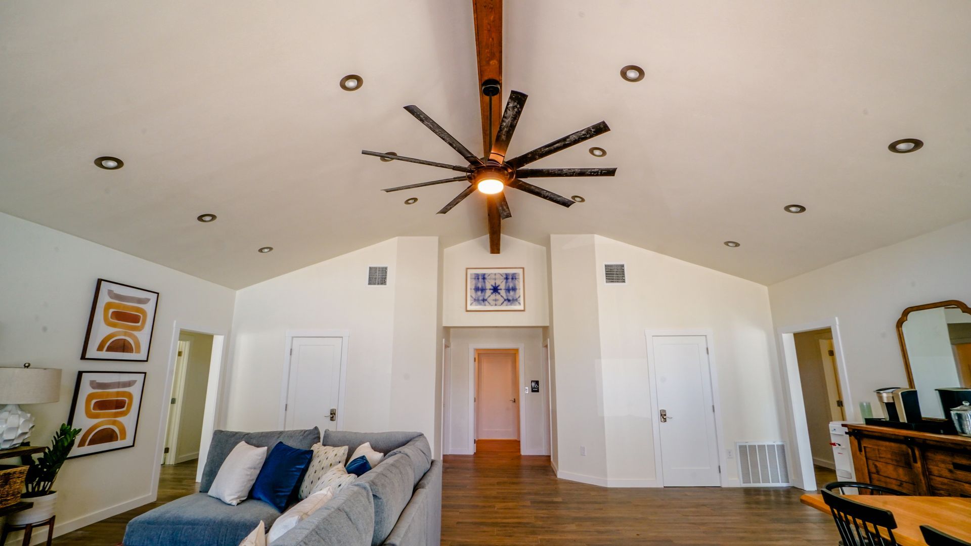 Living room with a high ceiling, a large fan, and recessed lighting. A couch is in the foreground.