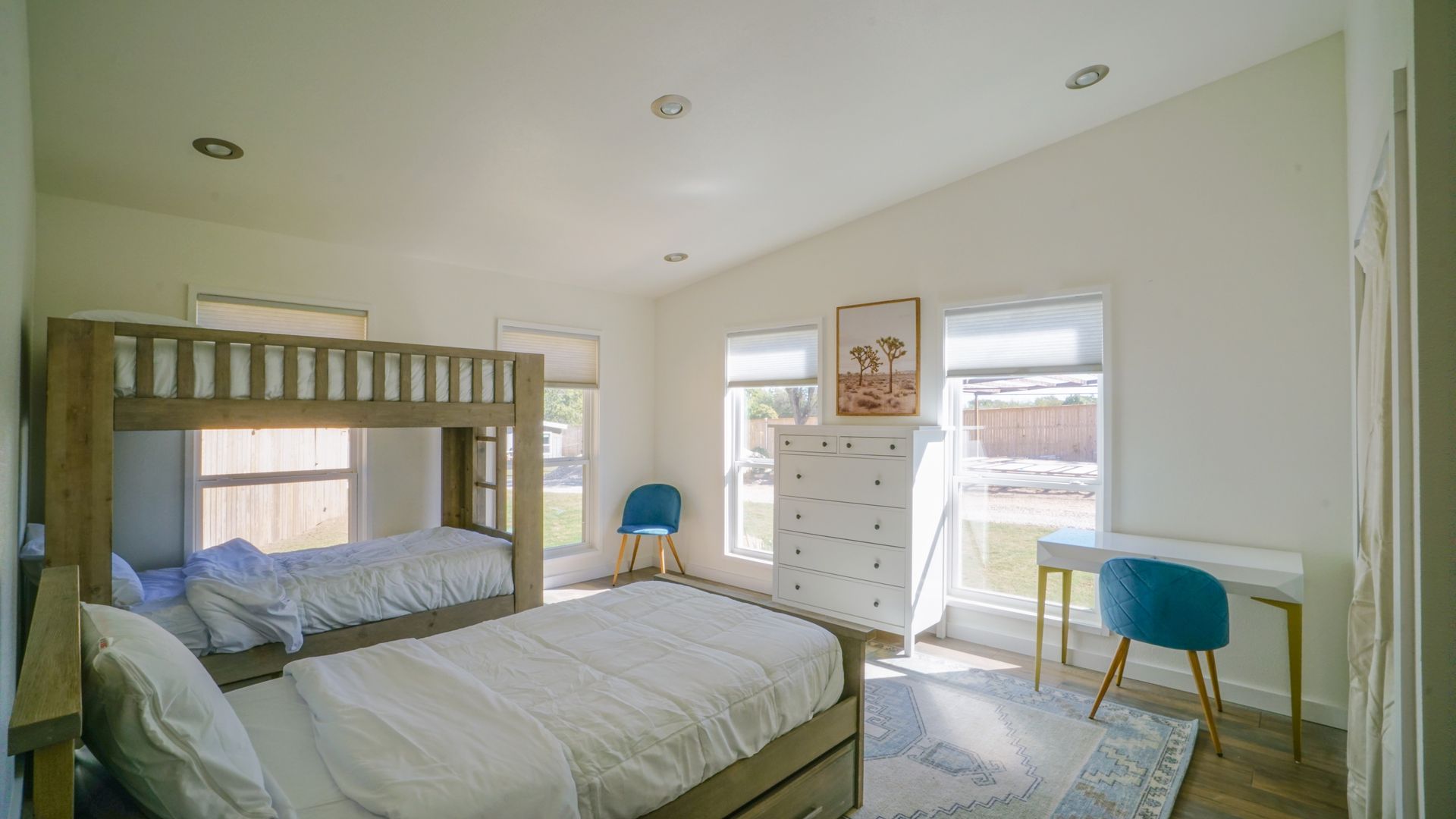 Bedroom with bunk beds, white walls, two windows, and a desk.