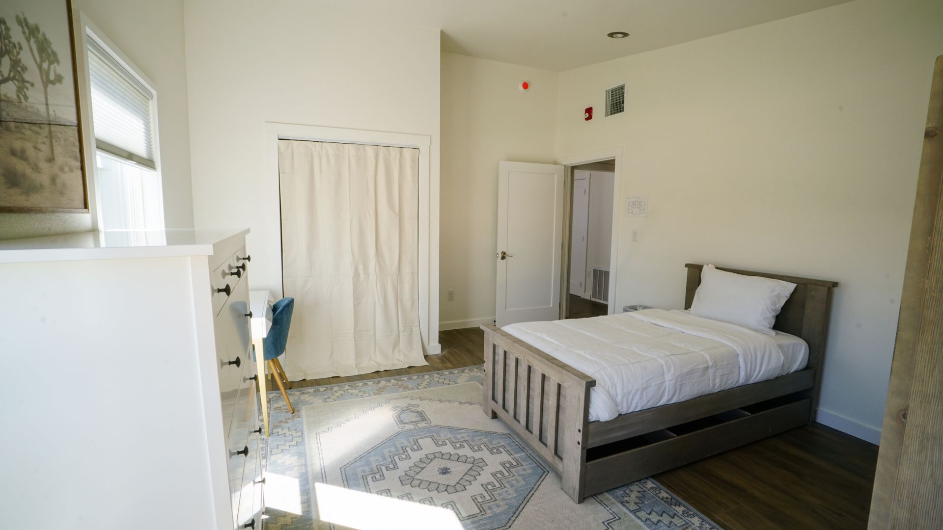 Bedroom with white walls, a bed, a dresser, and a door to a bathroom.