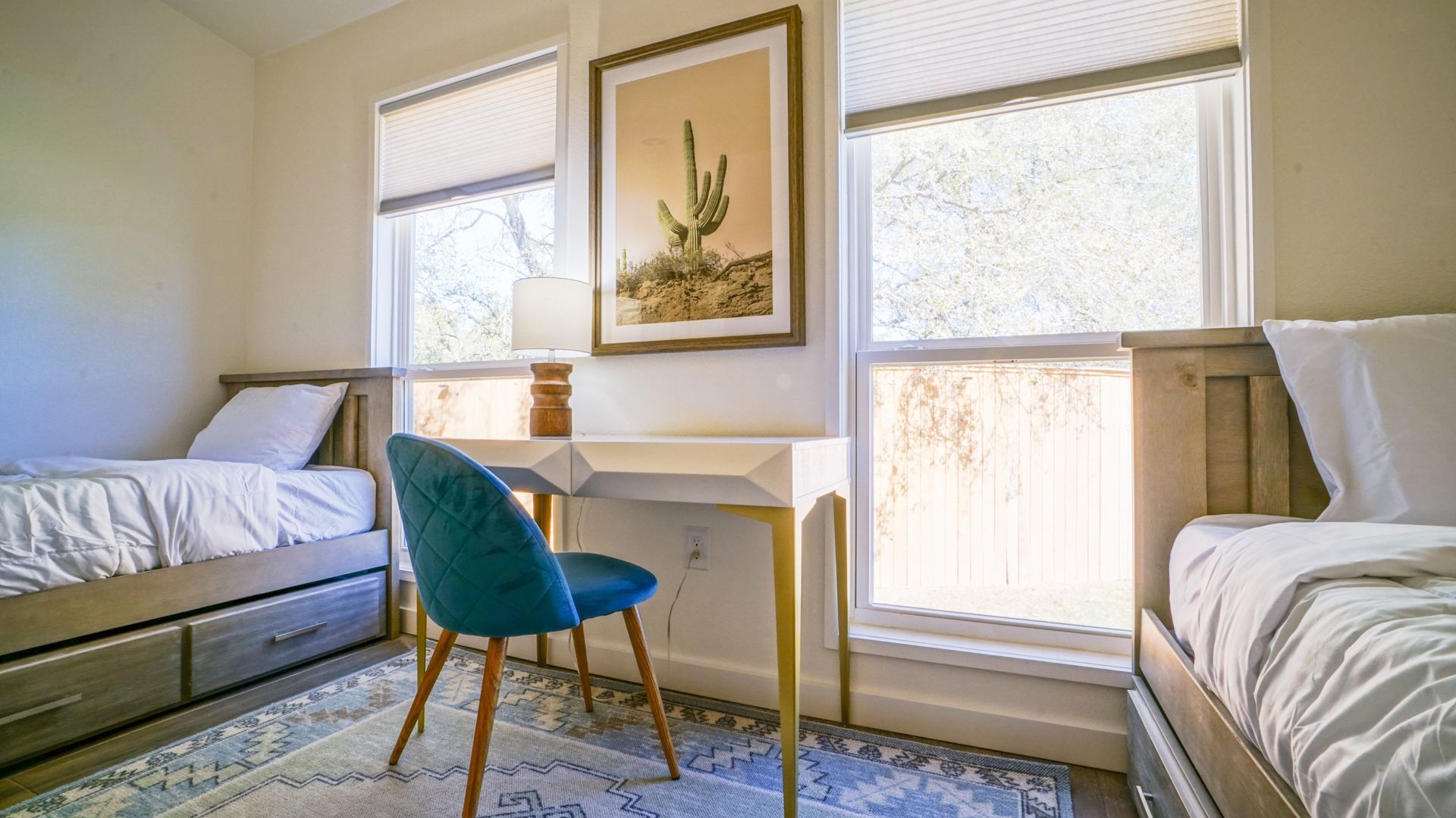 Bedroom with two twin beds, desk with chair, artwork, and windows.