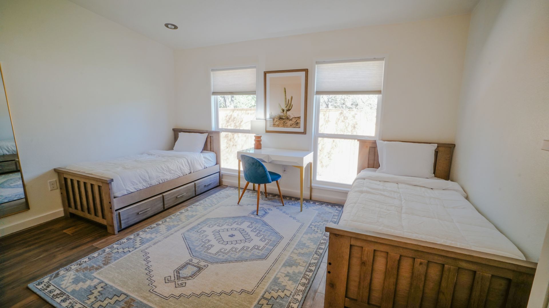 Two beds in a bright room with a desk and rug.