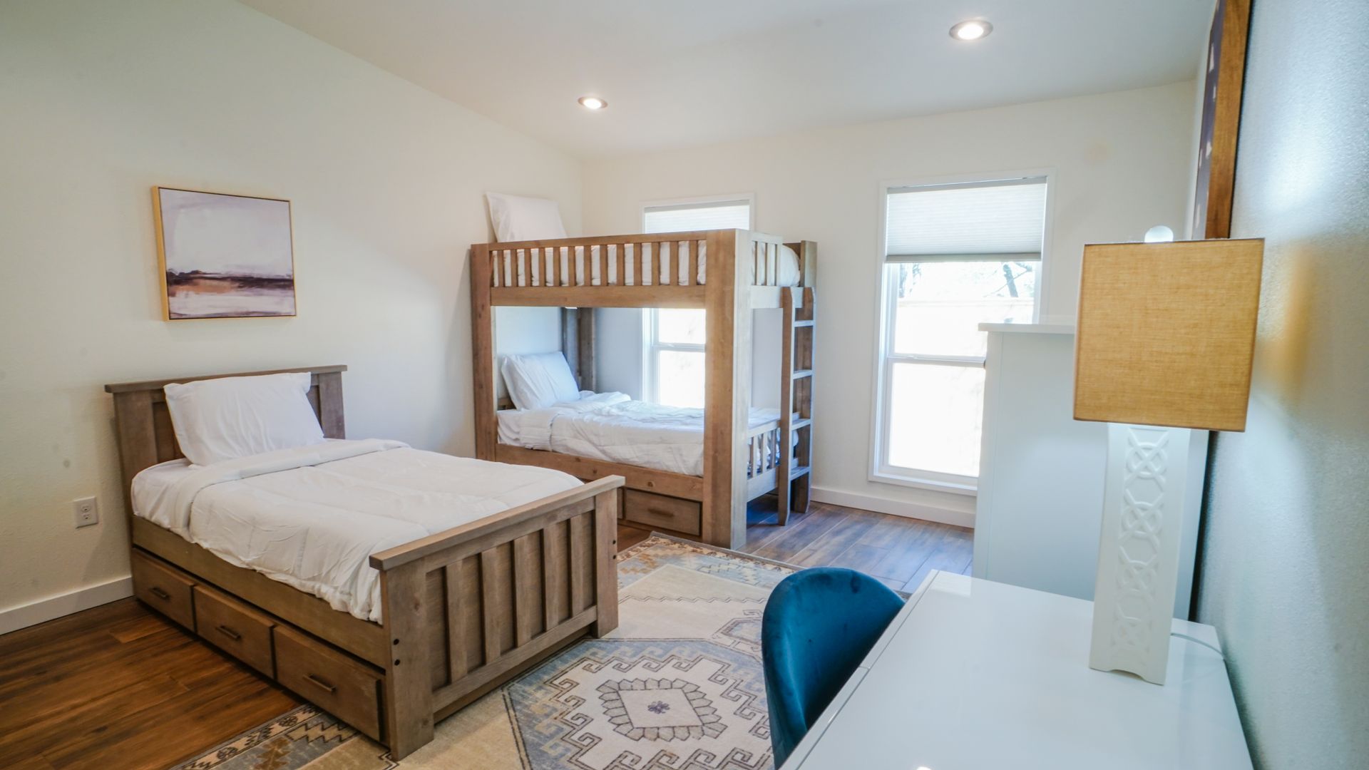 Bedroom with bunk beds, single bed, desk, and rug. Light wood furniture on wood floors.