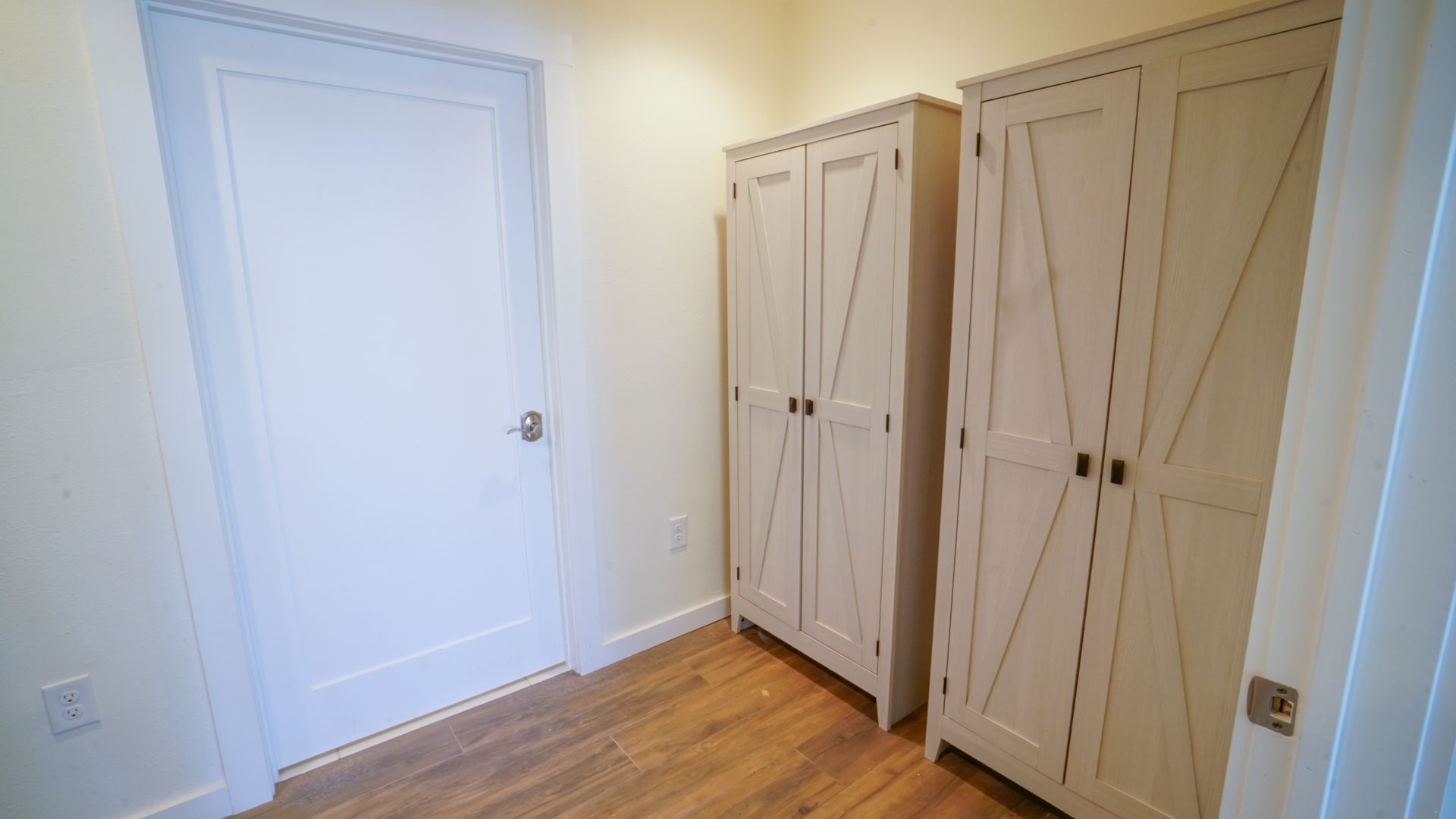 Two white cabinets and a white door in a room with wood flooring.
