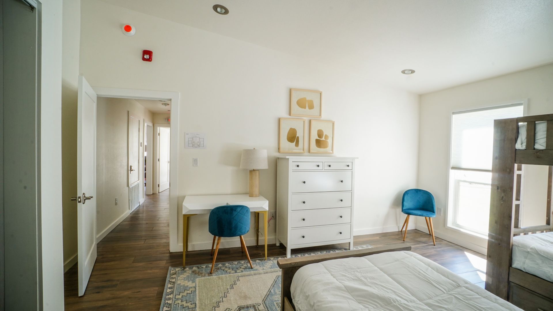 Bedroom with white walls, bunk beds, desk, dresser, and blue chairs.
