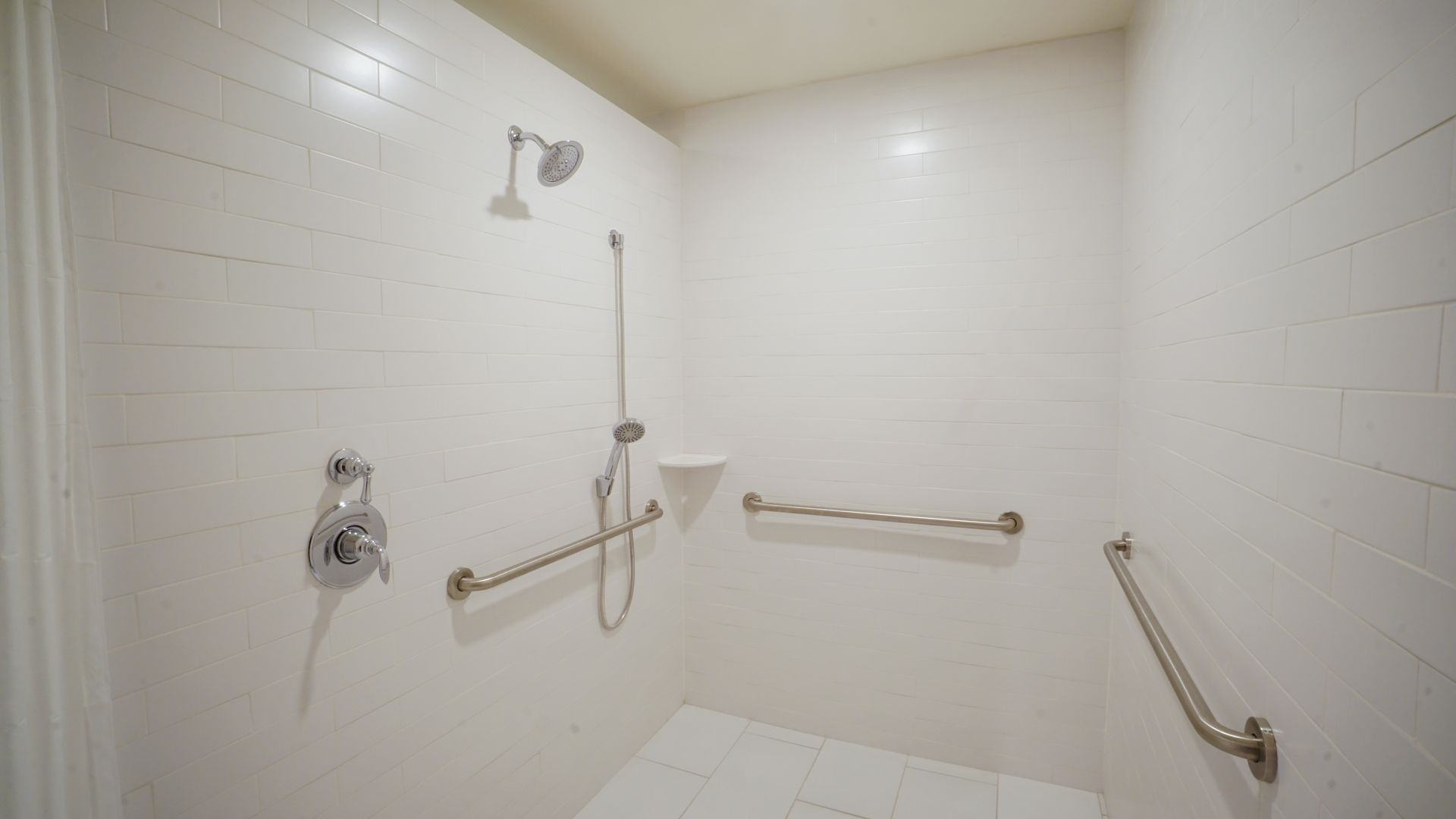 White tiled handicap-accessible shower with handrails, showerhead, and a soap dish.
